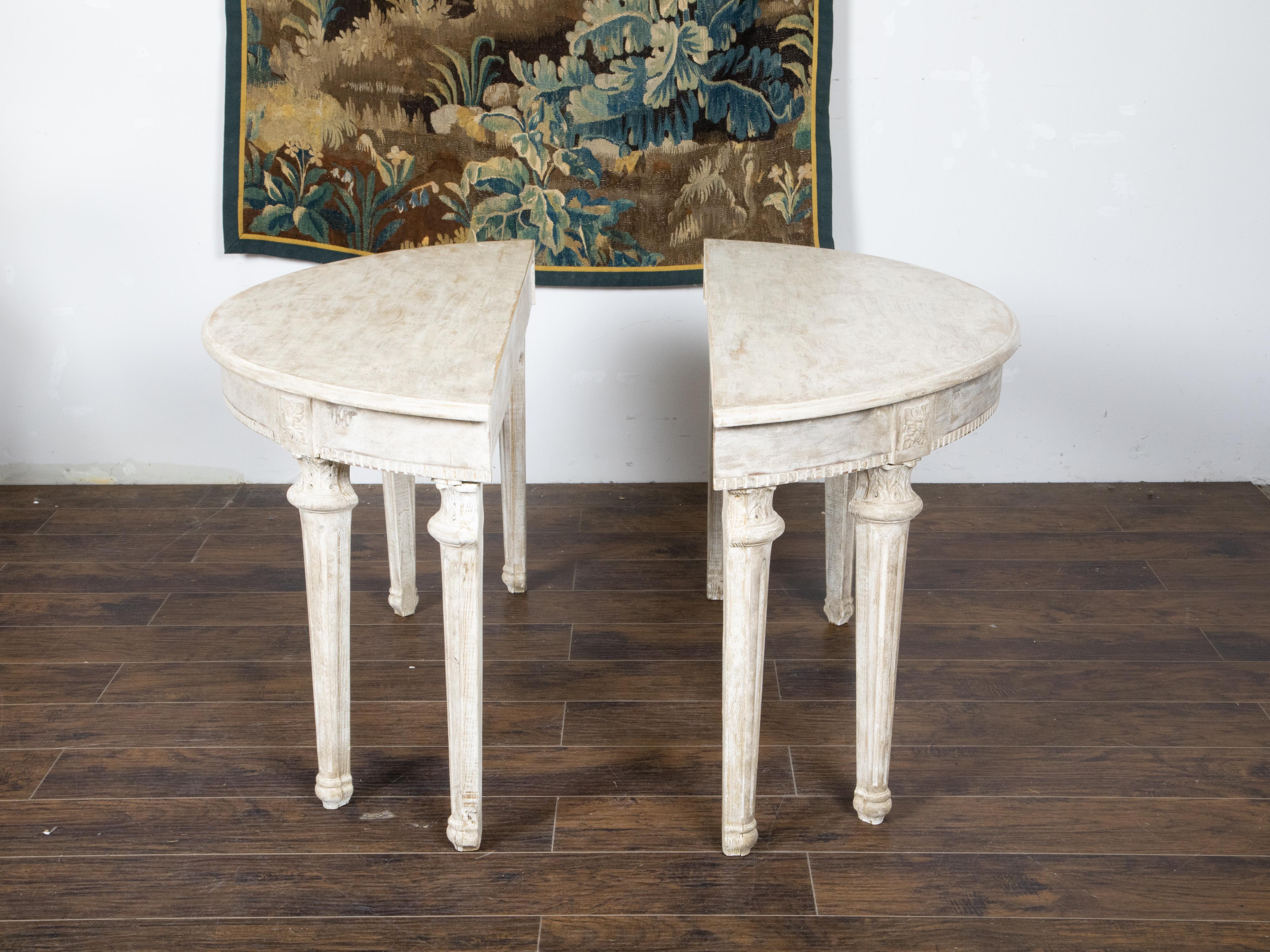 A pair of French Neoclassical style painted wood demilune console tables from the late 19th century, with carved rosettes, fluted legs and acanthus leaves. Created in France during the last quarter of the 19th century, each of this pair of demilunes