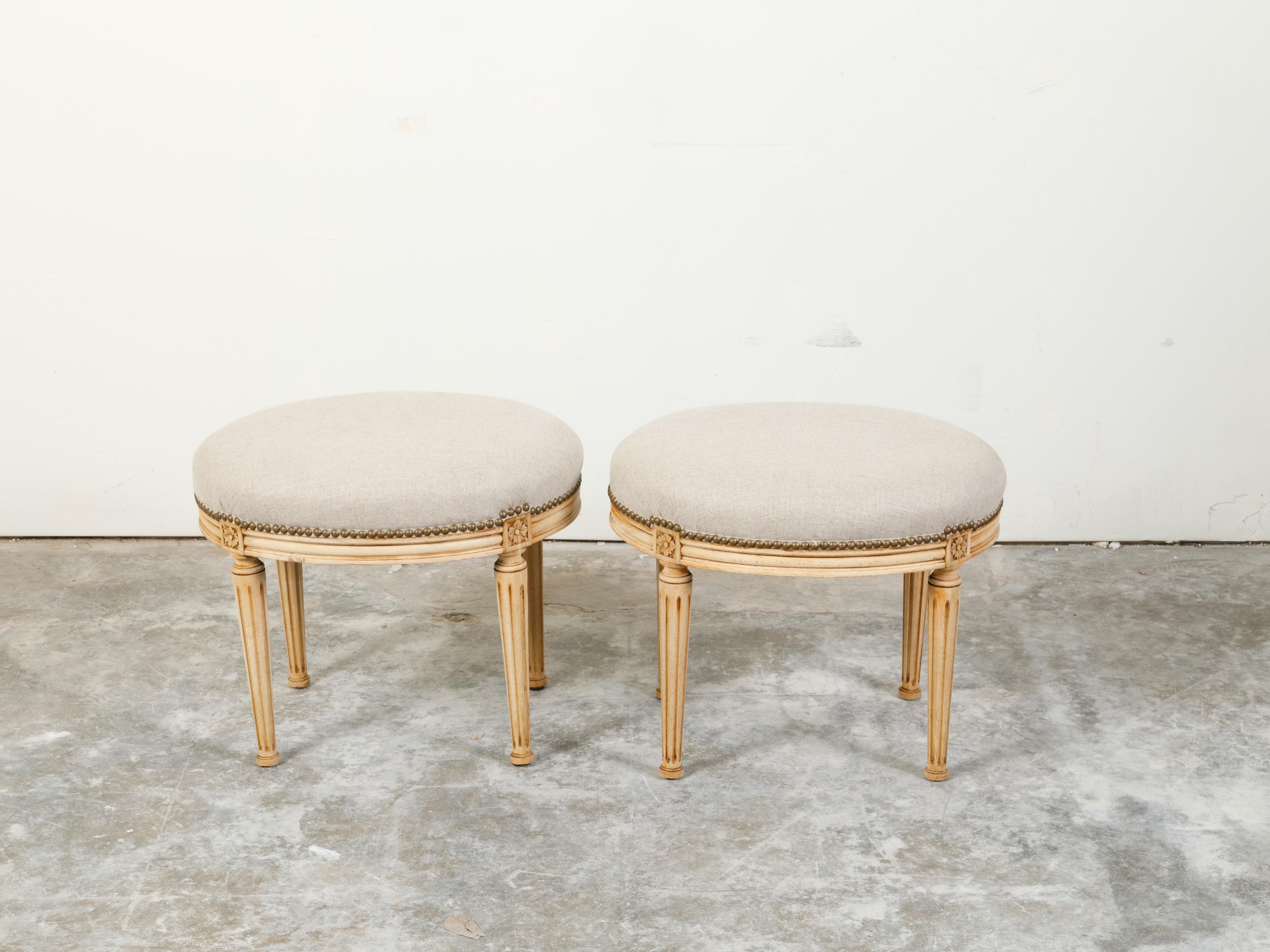 A pair of French neoclassical style bleached wood stools from the early 20th century, with fluted legs and new upholstery. Created in France during the second quarter of the 20th century, each of this pair of stools features a top newly