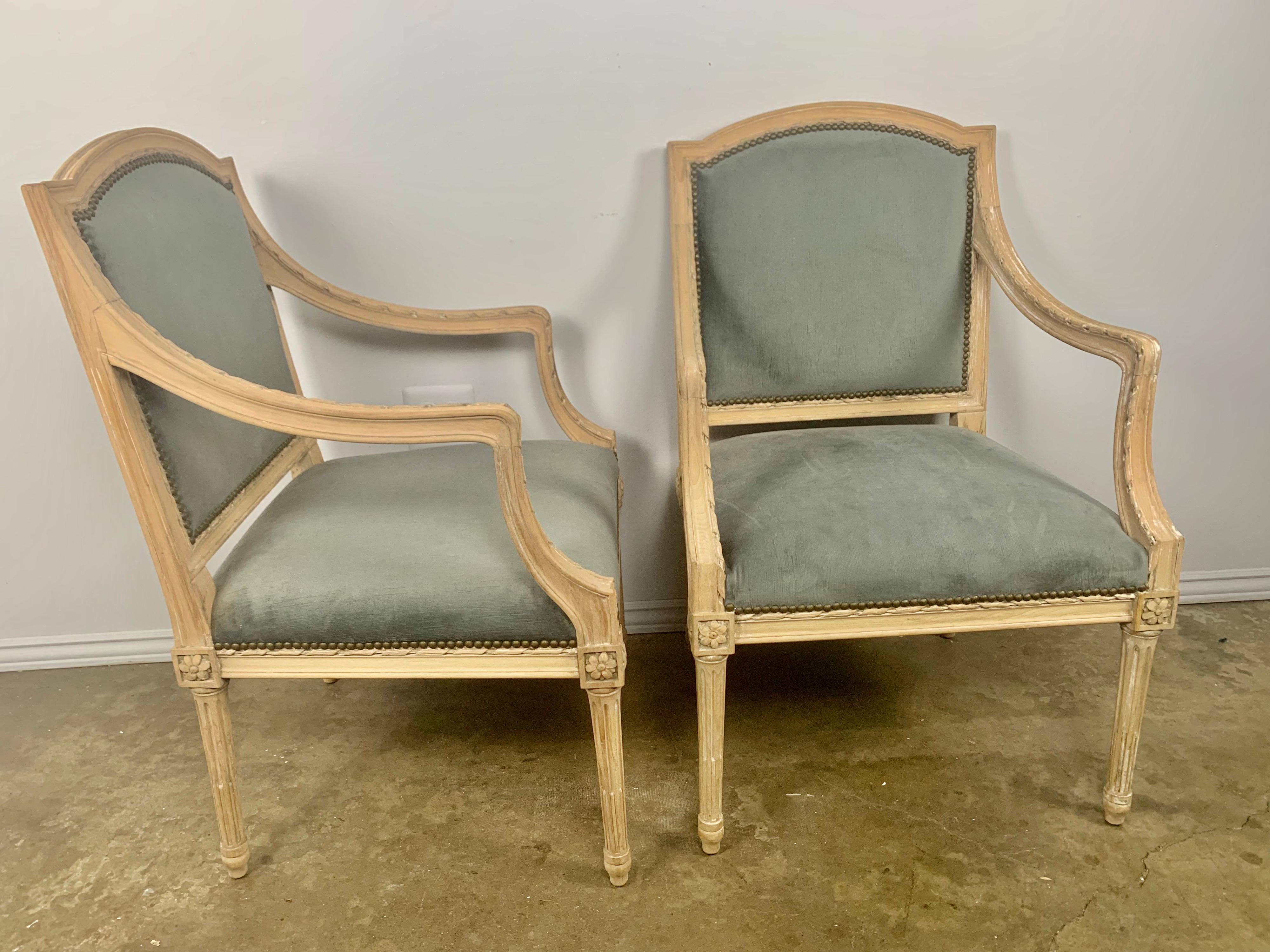 Pair of French Louis XVI style armchairs standing on four straight fluted legs. The chairs have been bleached and refinished. The armchairs are also newly upholstered in a steel blue colored velvet and are ready to install. Measure: 19