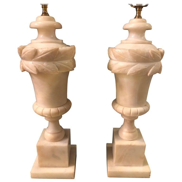 A very elegant pair of alabaster urn shaped tables lamps in an off white. Each lamp is raised by a square pedestal base and feature two sumptuous omulu bands. The pair of the French neoclassical lamps would be a lovely addition to any living