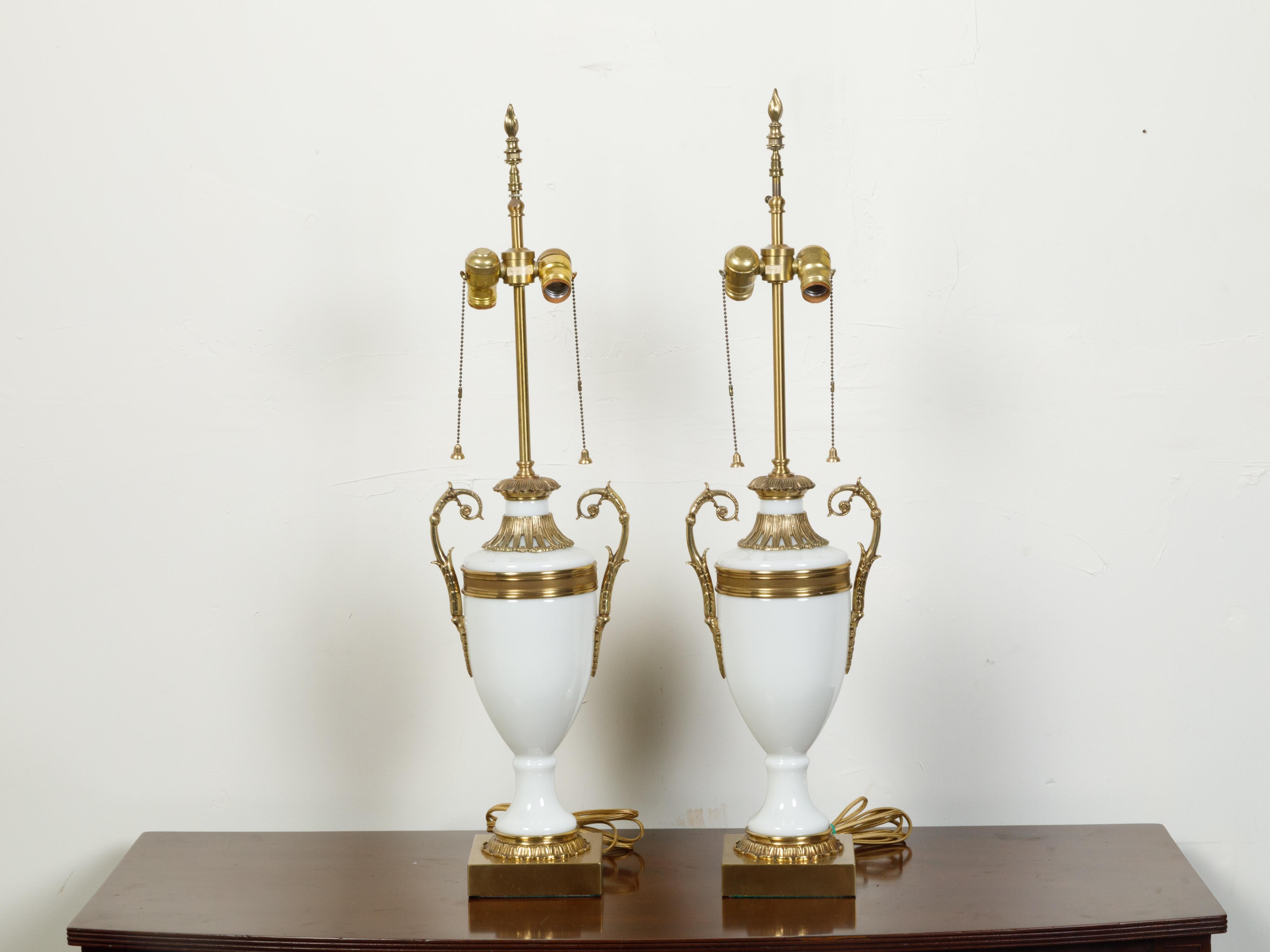 A pair of French Neoclassical style opaline glass urn-shaped table lamps from the 20th century, with brass accents. Created in France during the 20th century, each of this pair of table lamps captures our attention with its Classical urn-shaped