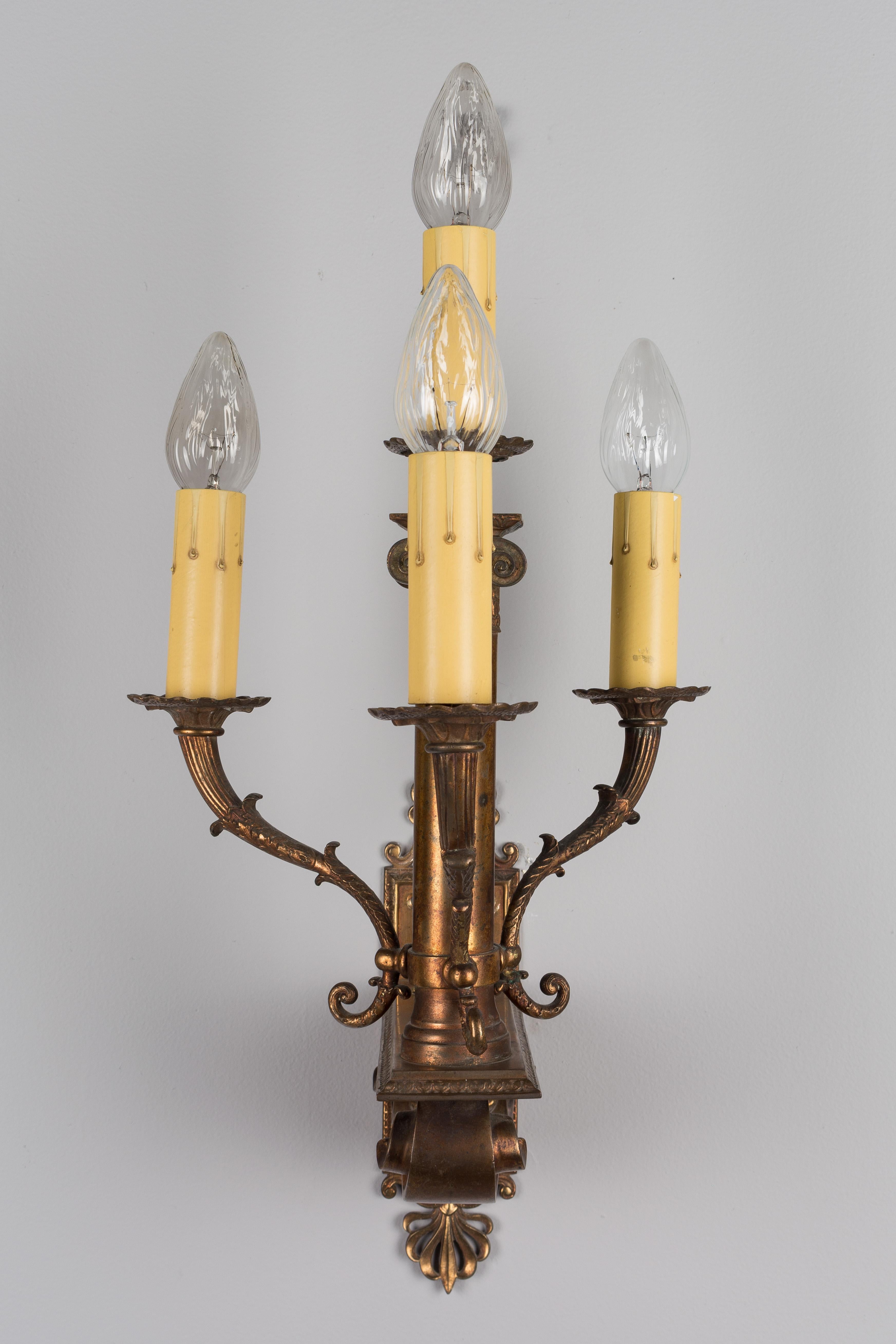 A pair of French neoclassical style four-light brass sconces with copper patina. Central ionic column with three arms all resting on large plinth with scroll motif attached to a rectangular backplate. Wired, but  should be checked by an electrician.