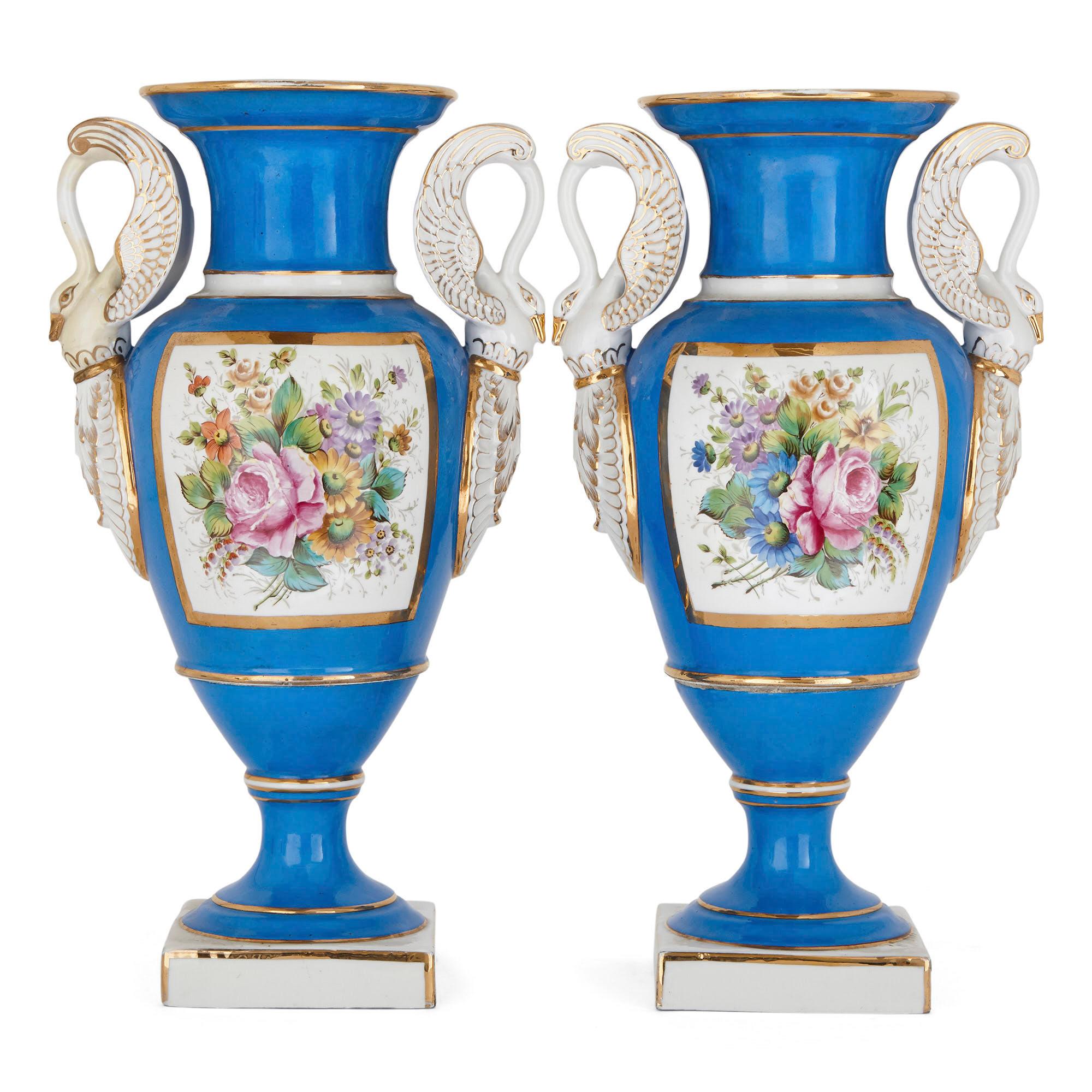 This pair of comprises pendant krater-shaped porcelain vases. Each vase’s wide-lipped ovoid body is supported by a flared stem, which stands on a square-sided podium. Most strikingly, each vase in the pair is mounted with two porcelain swan necked