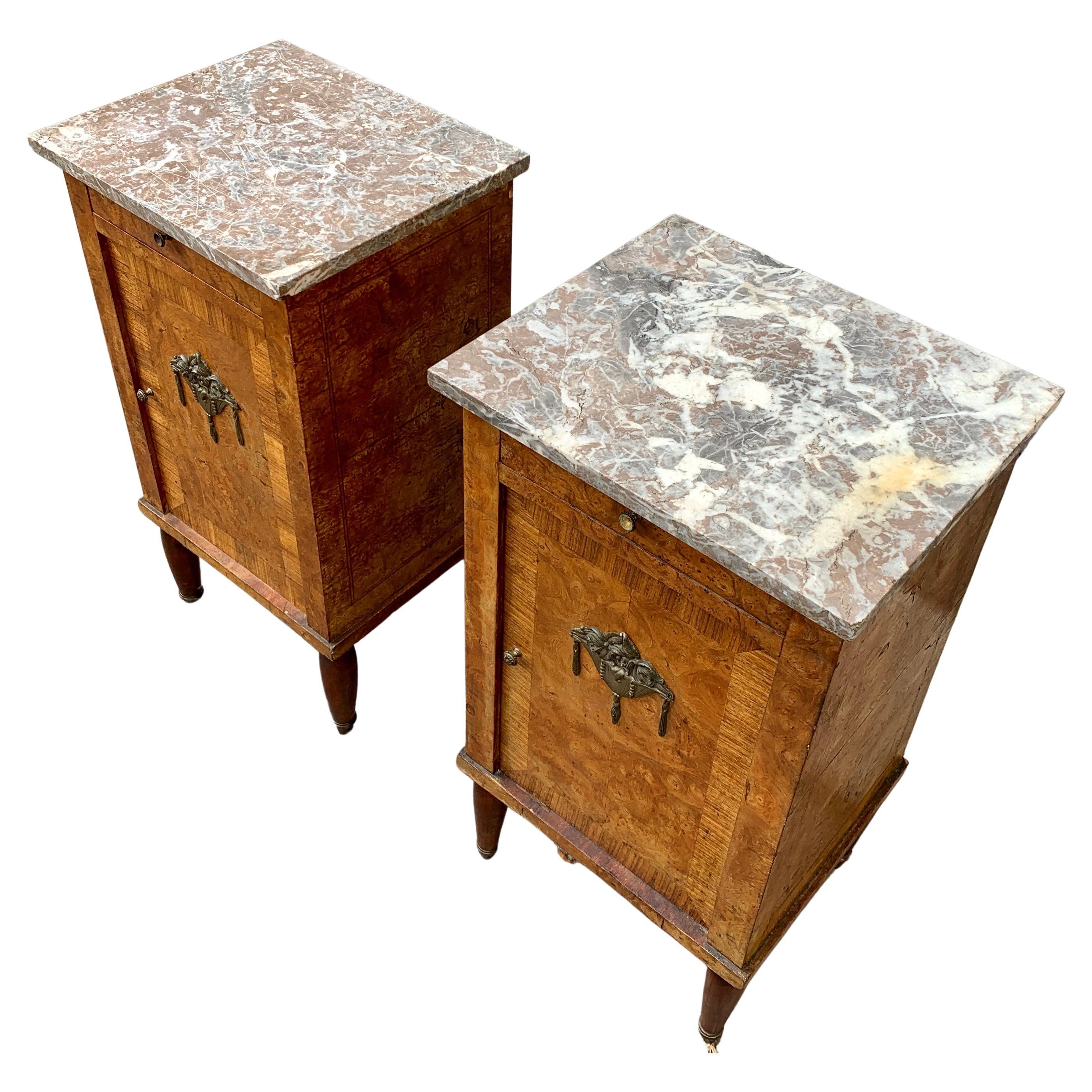 A pair of early 20th Century French nightstands or night tables in walnut, walnut root and citrus wood with marquetry work. The french marble tops are loose. That will not effect stability when put on the nightstands cause their weight keep them