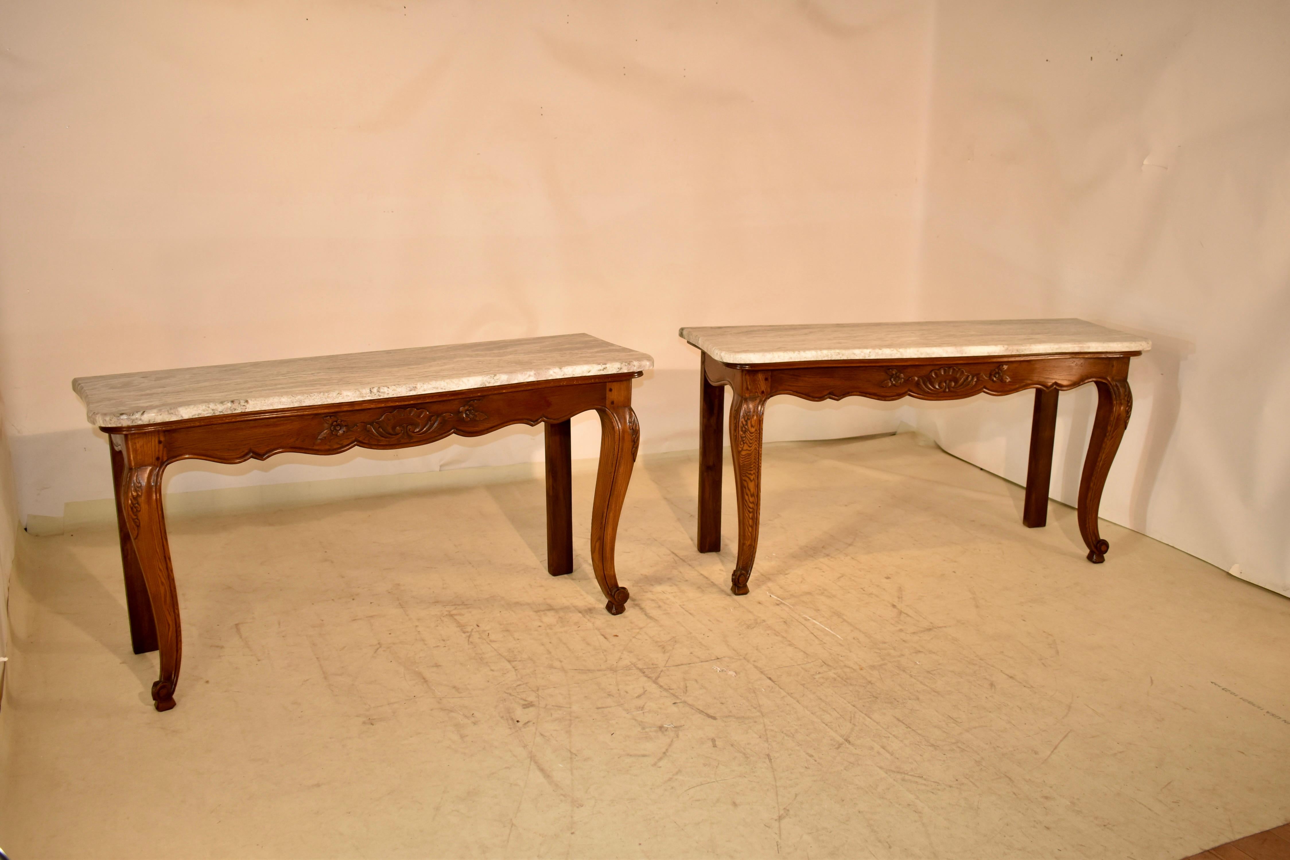 Coppia di consolle in Oak provenienti dalla Francia con piani in marmo.  I piani sono smerlati intorno al bordo per rispecchiare le basi.  Le basi hanno splendidi grembiuli intagliati a mano e smerlati, tutti con struttura a pioli.  I tavoli sono