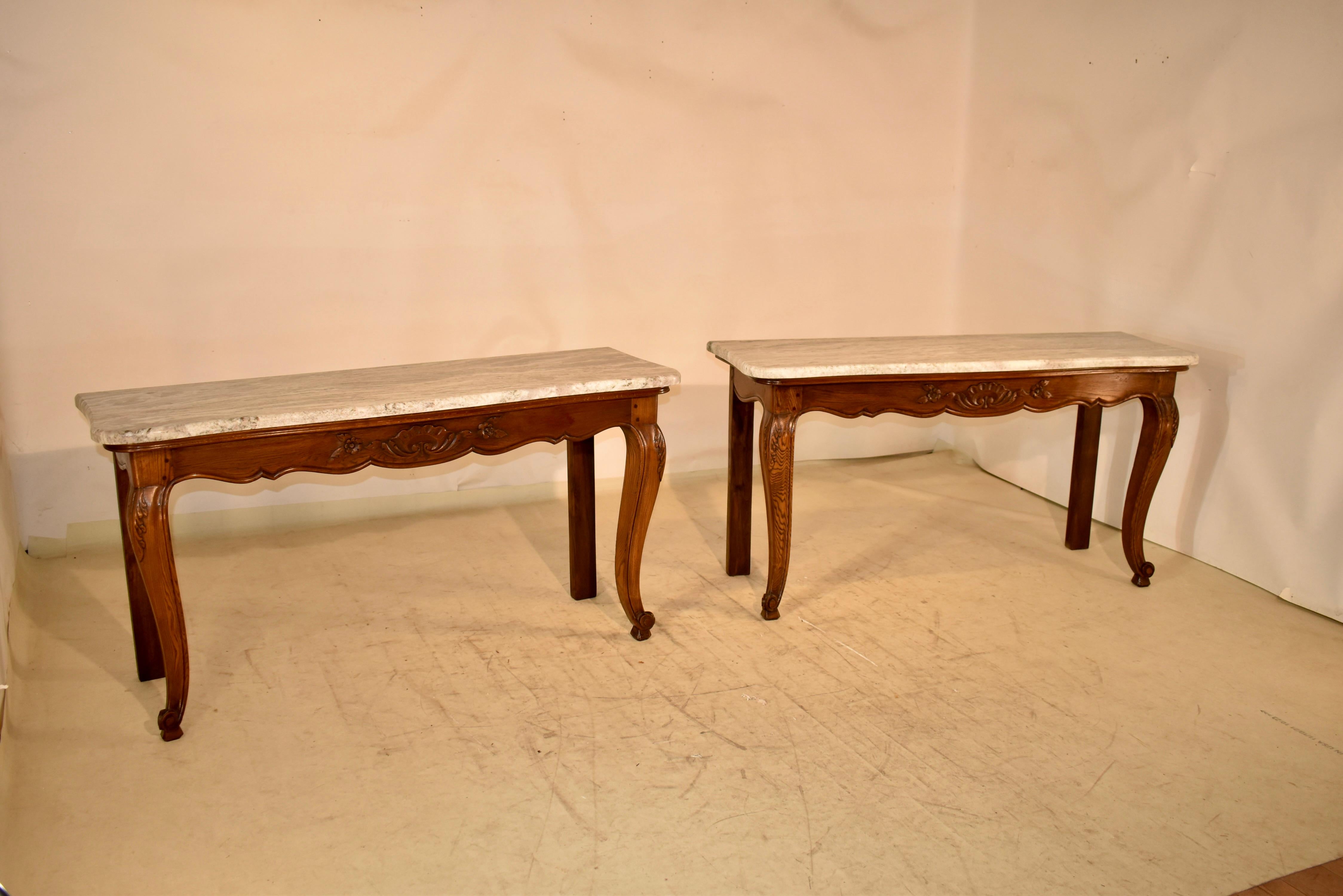 Pair of oak consoles from France with marble tops.  The tops are scalloped around the edge to mirror the bases.  The bases have gorgeous hand carved and scalloped aprons, all with pegged construction.  The tables are supported on simple legs in the