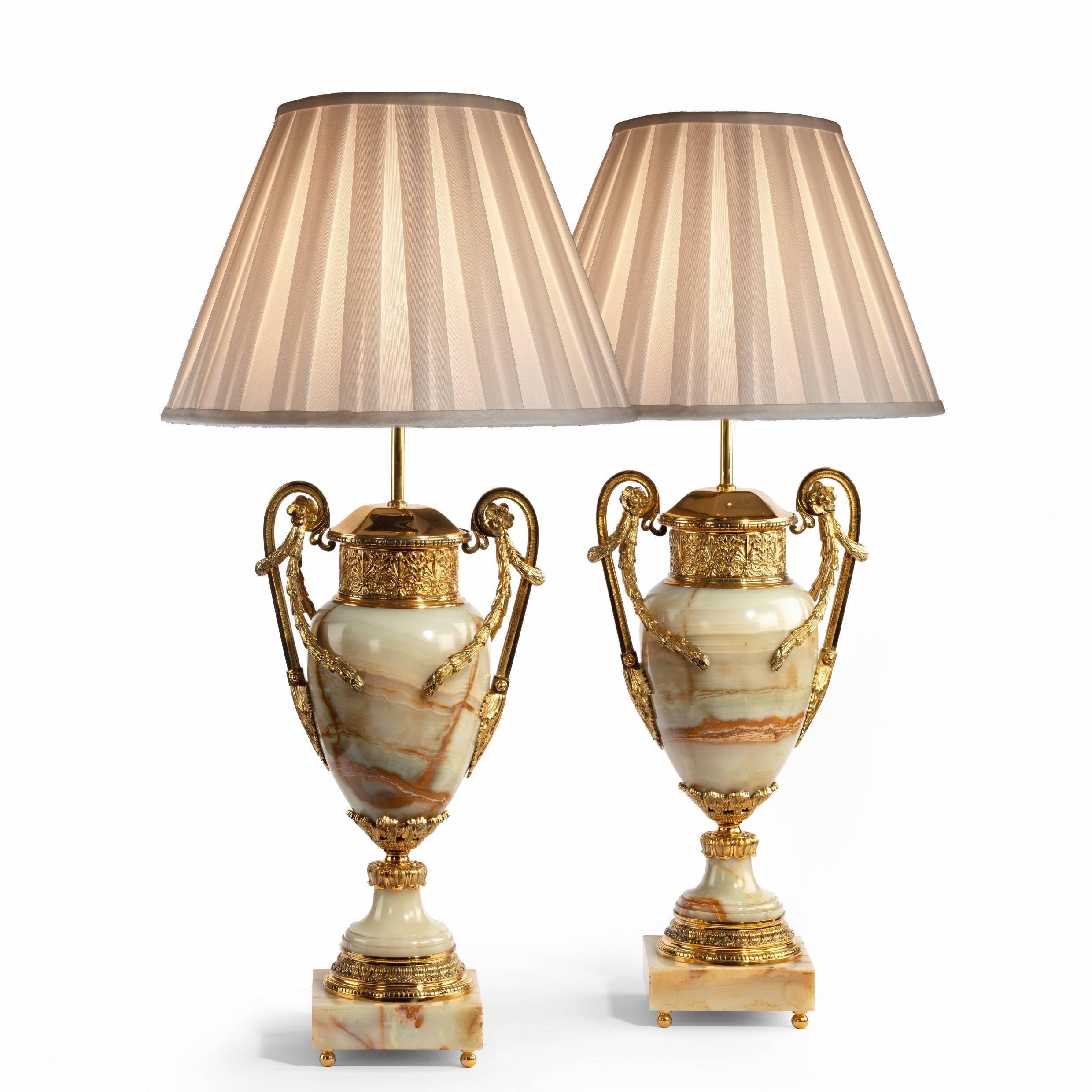 An impressive pair of French onyx and ormolu lamps, each in the form of a classical urn decorated with lavish ormolu mounts comprising a high scroll handle draped with rosettes and garlands, a wide collar at the neck and bands of classical motifs.