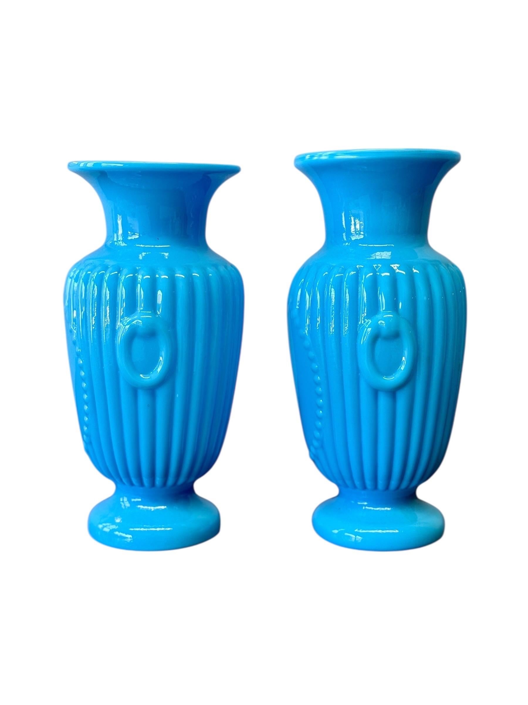 A striking pair of 19th-century French opaline glass vases in a rare and vibrant turquoise blue. Each vase features a finely moulded neoclassical shape with fluted decoration, beaded medallions, and applied ring handles on the sides. The opaline