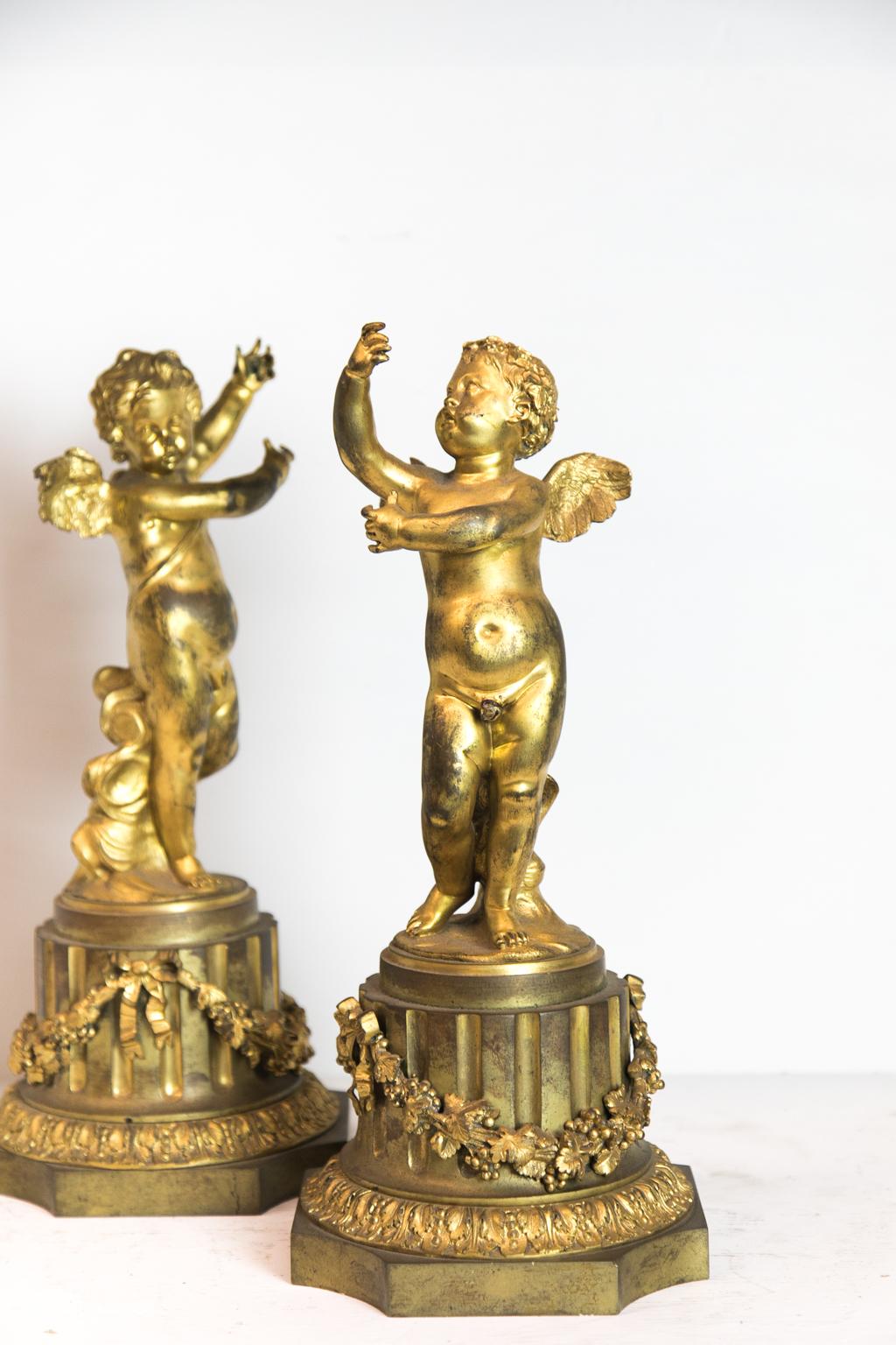 Pair of French ormolu cupids, standing on a fluted column base draped with grapevine swags and acanthus base molding.