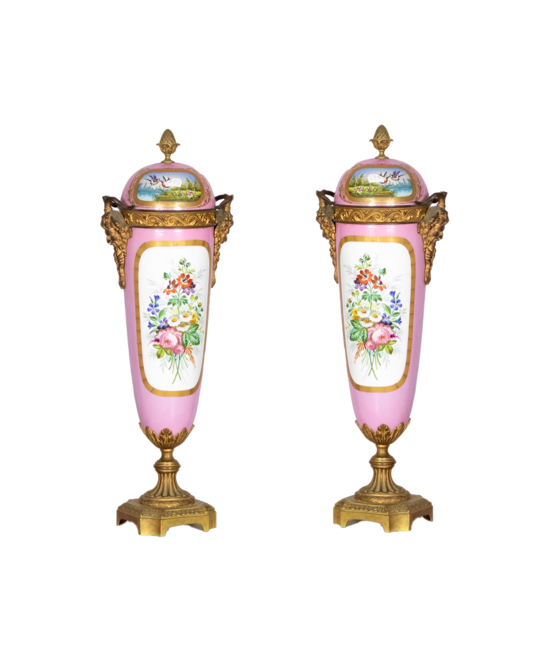 Una bella coppia antica di urne decorative in porcellana rosa in stile Sèvres con uno sfondo dipinto a mano di una scena di innamorati. 

Sul retro c'è una scena di un bouquet di fiori. Maniglie della maschera di bronzo di Bacco/Dioniso montate sui
