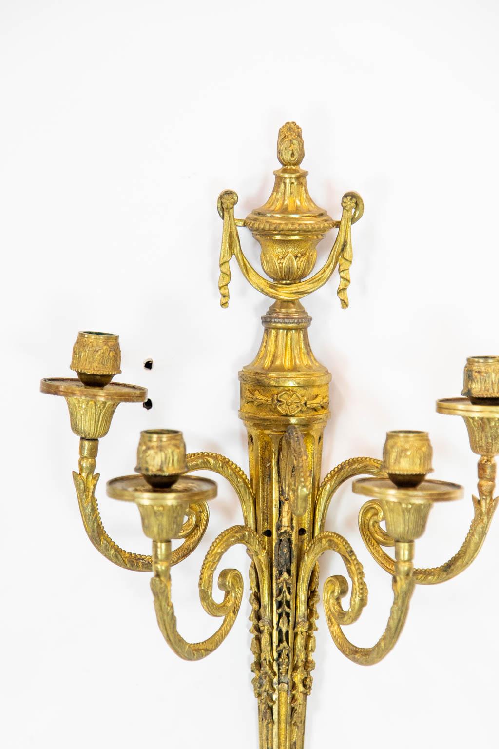 Each of these wall sconces has four candle sockets and a fluted central section with carved grapevines and leaves. The top has a classical with drapery swags.