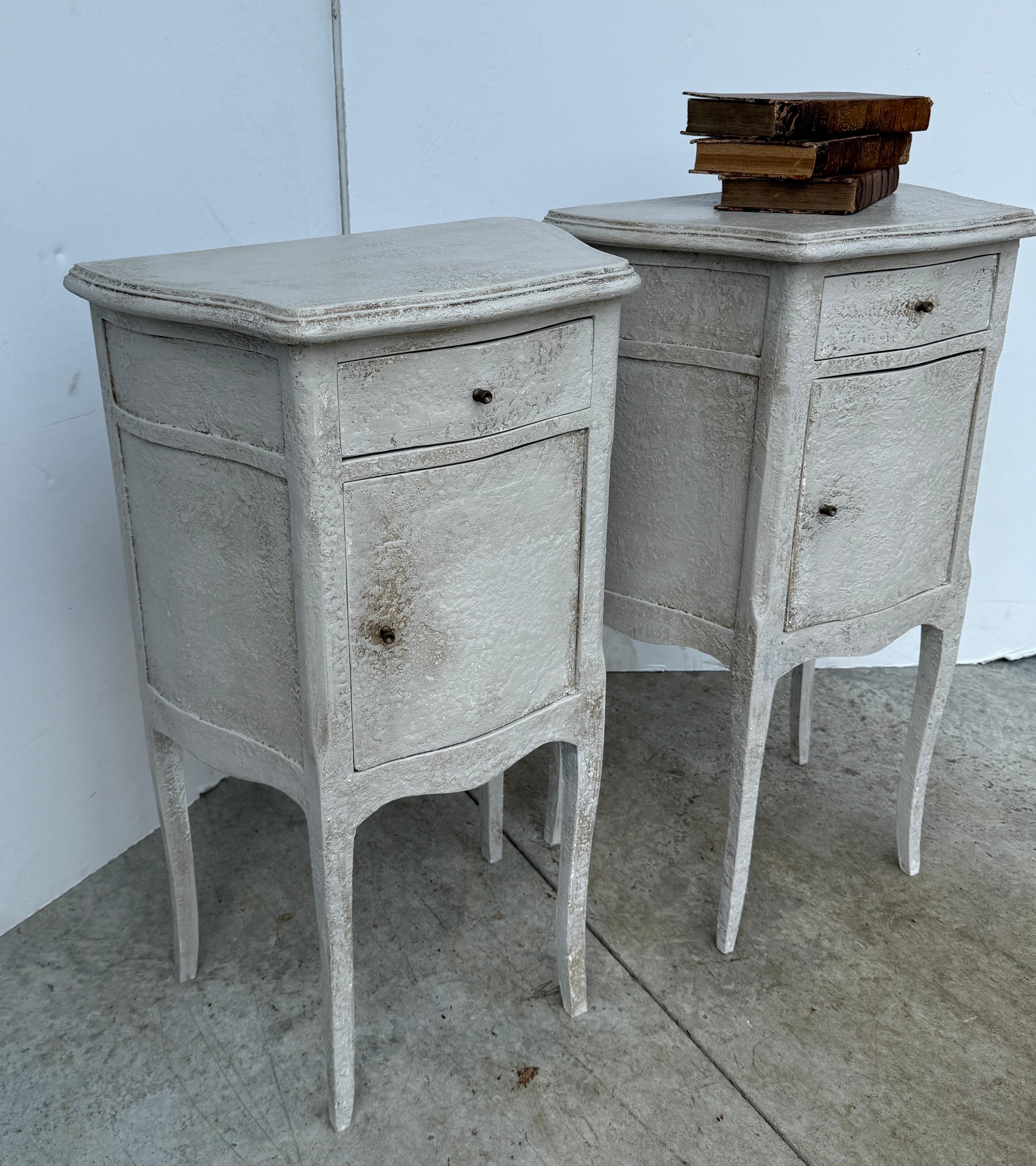 This pair of French nightstands or bedside tables is made in solid wood and have been painted in a light neutral Gustavian gray cream color with rich thick patina, Classic details on this set including brass hardware with a hand-applied finish. This