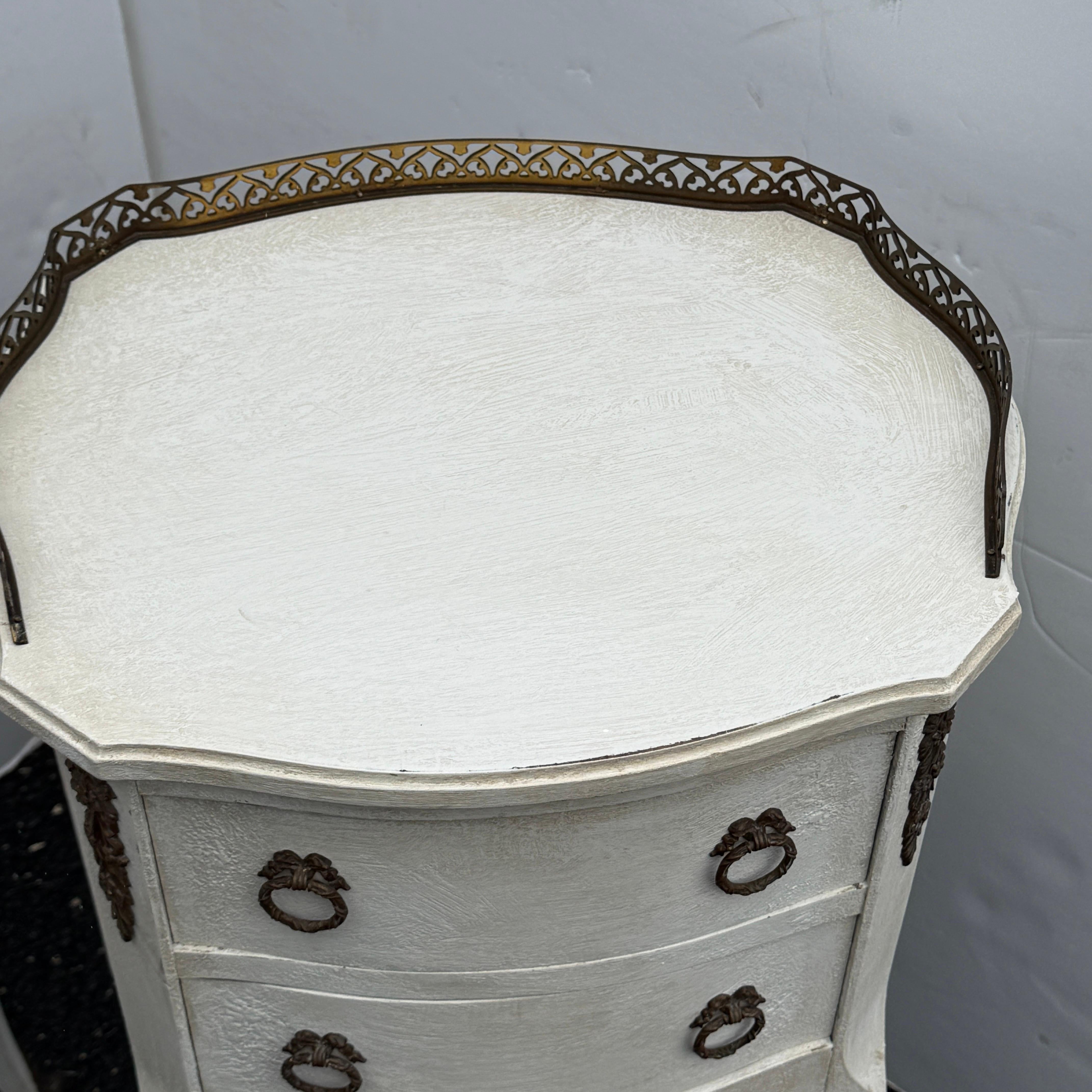 This pair of French two drawer nightstands or bedside tables have been constructed from solid wood and have been painted in a light neutral gray cream color. Classic details on this set including brass rails and hardware with a hand-applied finish.