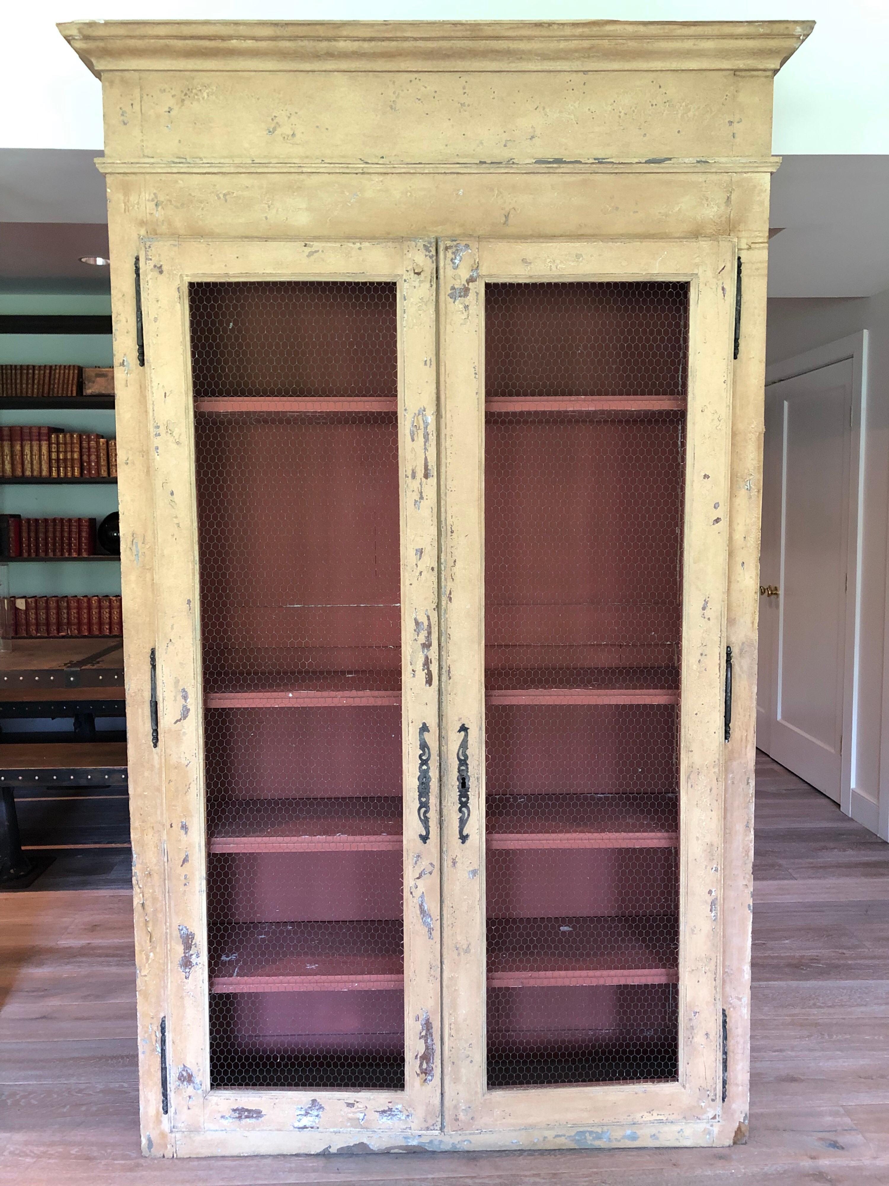A pair of French provincial painted wood cabinets or cupboards. Each with four adjustable shelves, wire front doors and brass hardware. Measurements are from largest top molding. Sold individually.