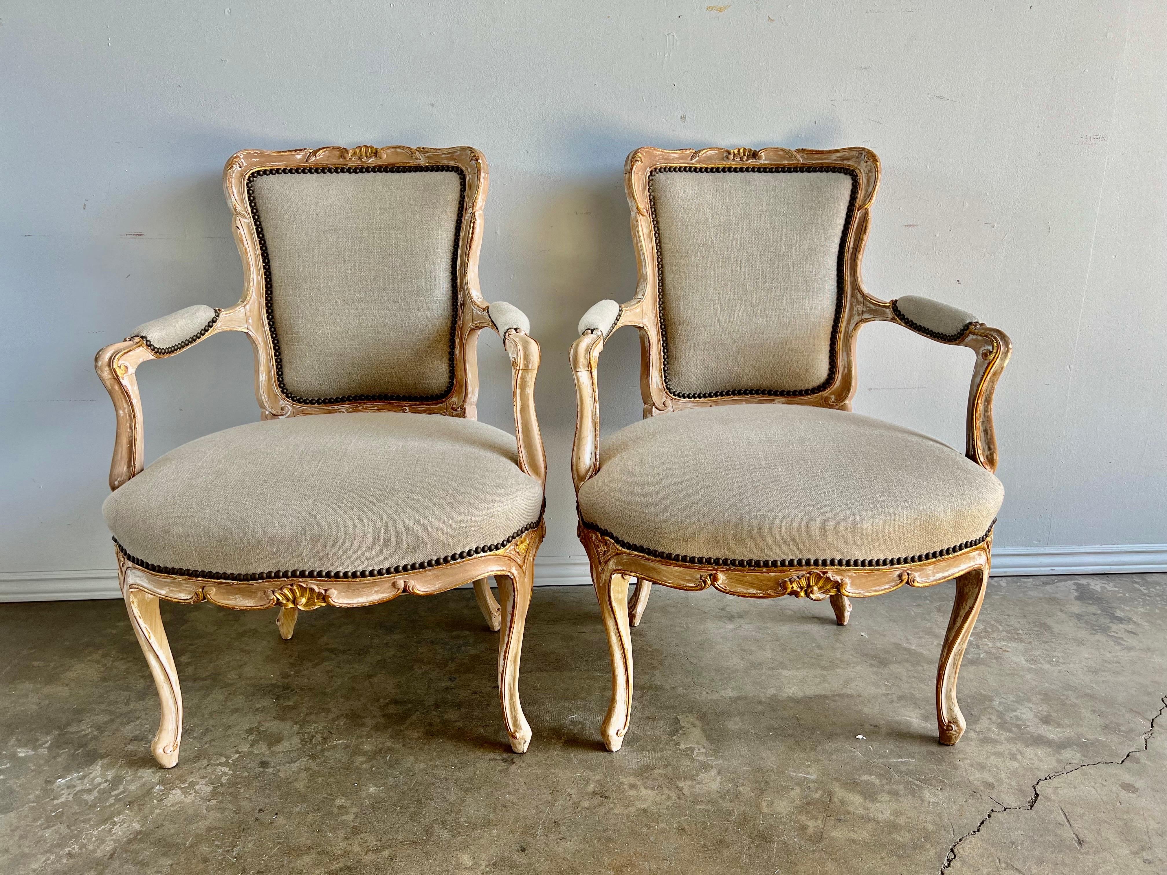 Pair of French painted & parcel gilt Louis XV armchairs newly upholstered in a washed Belgium linen with nailhead trim detail. Worn and missing paint and gold leaf throughout.