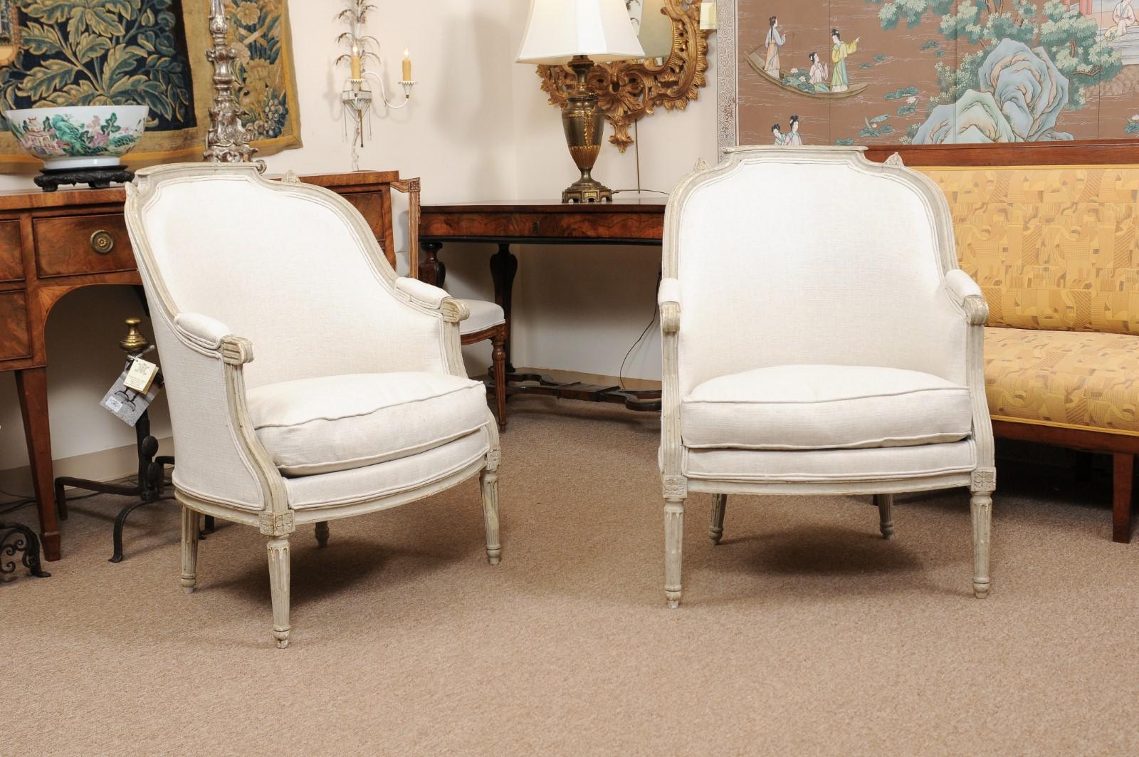 A pair of Late 18th century Louis XVI French painted Bergeres in a pale green hue with rounded backs, linen upholstery and carved fluted turned legs.
