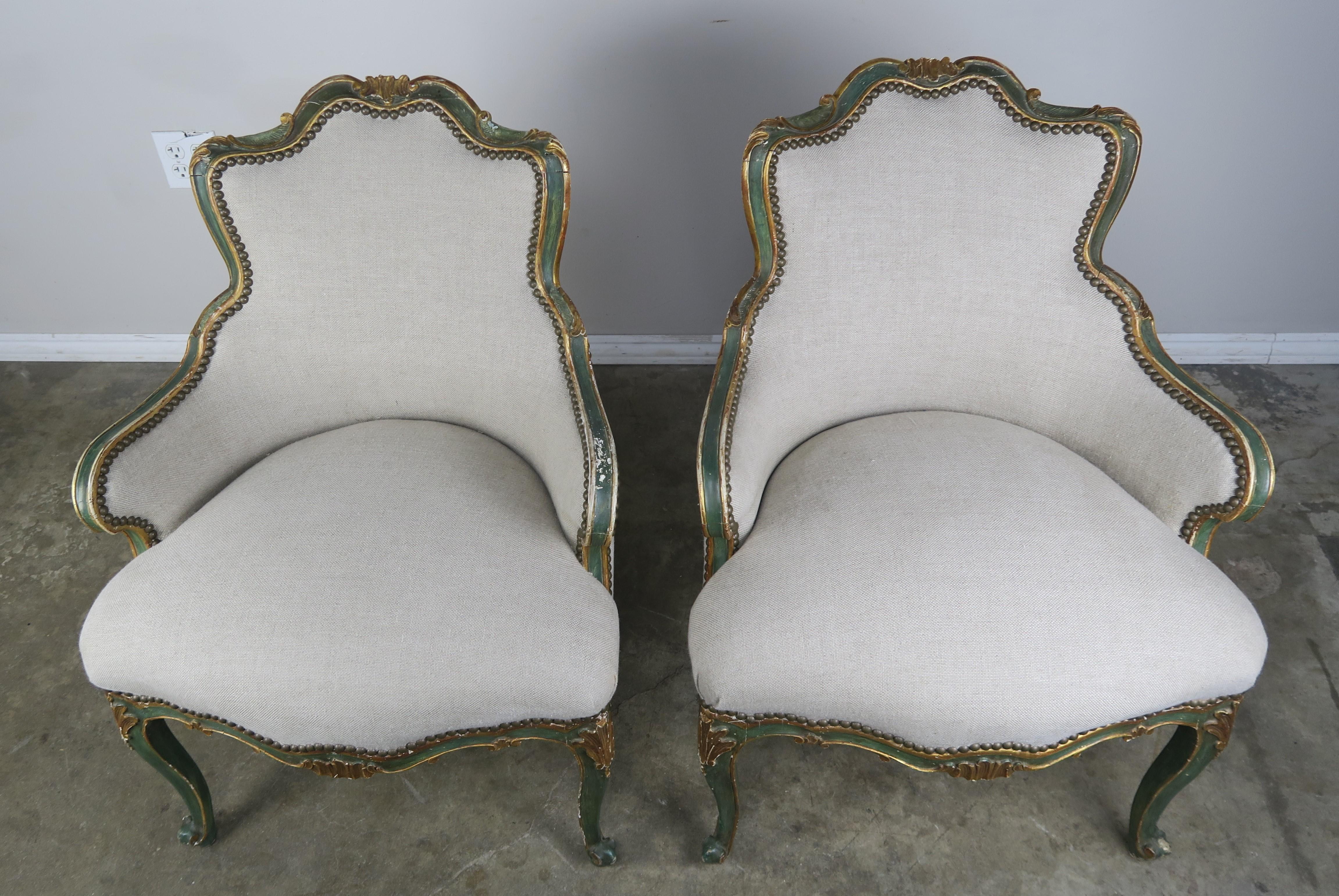 Pair of French painted and parcel gilt accent armchairs with beautifully shaped backs. The chairs Stand on four cabriole legs that end in ram's head feet. The chairs are newly upholstered in a washed Belgium linen with antique brass colored nailhead