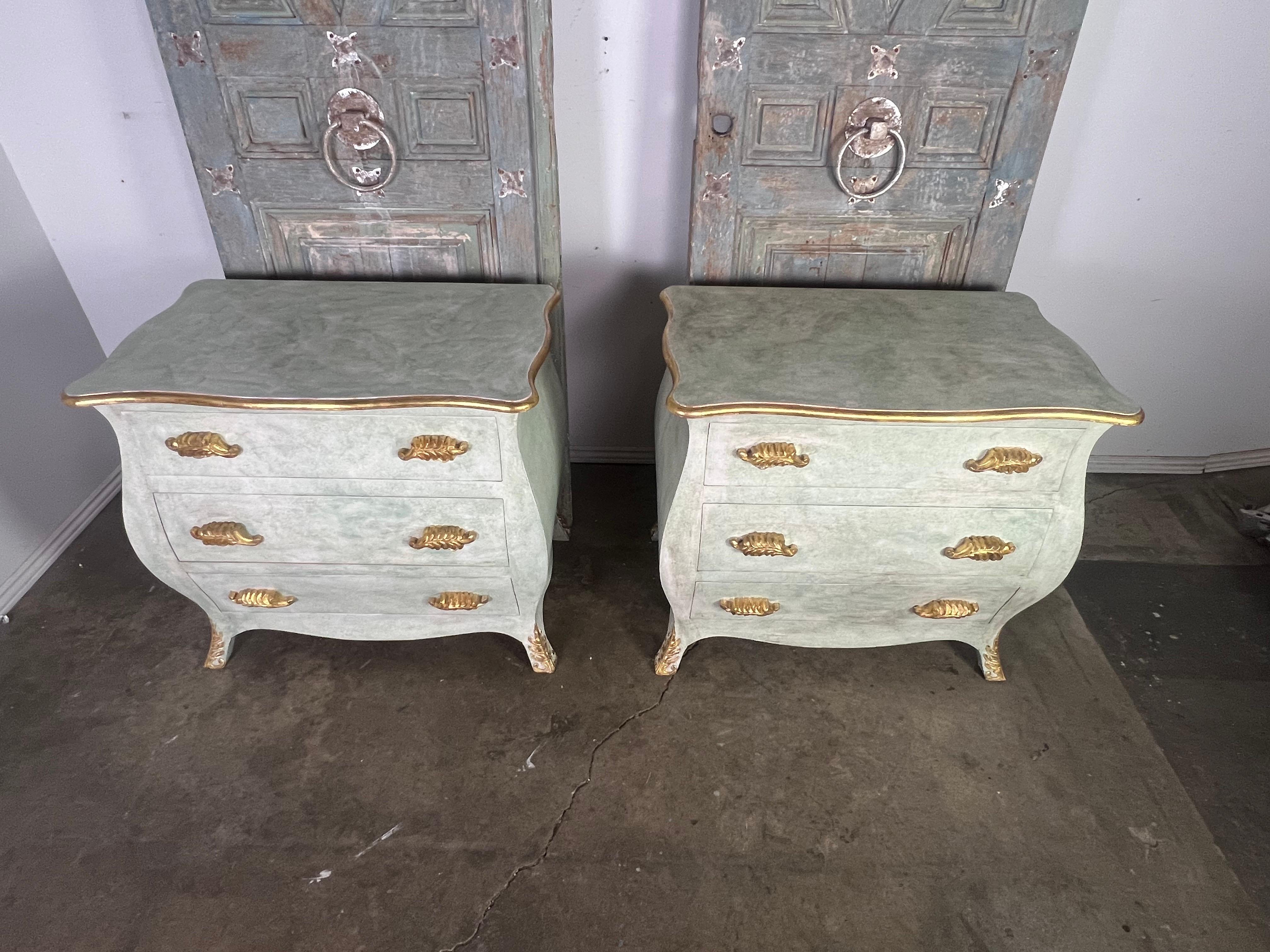 Pair of finely made painted & parcel gilt bombe chests.  They are painted in a soft faded green with antique painted finish. The dressers have a bombe-style shape, characterized by their outward curving sides.  The edges, feet, and wood handles are