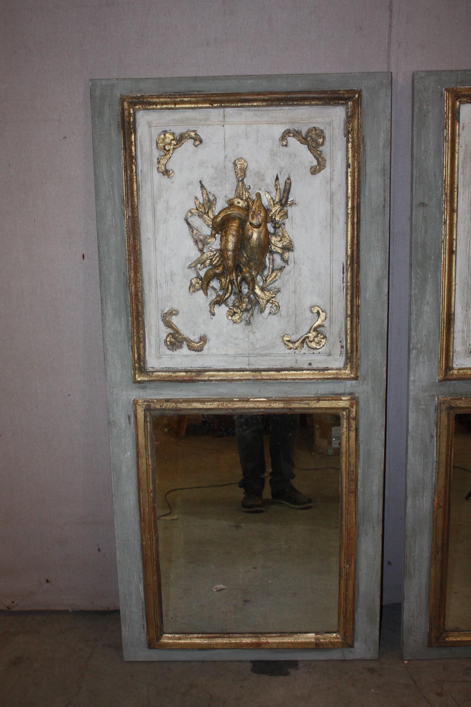 This is a very nice pair of French painted trumeau mirrors that dates to the late 1800s, early 1900s. One has a marine scene of caught fish and a lobster carved. The other has a woodcock carved. The gold is gilded.