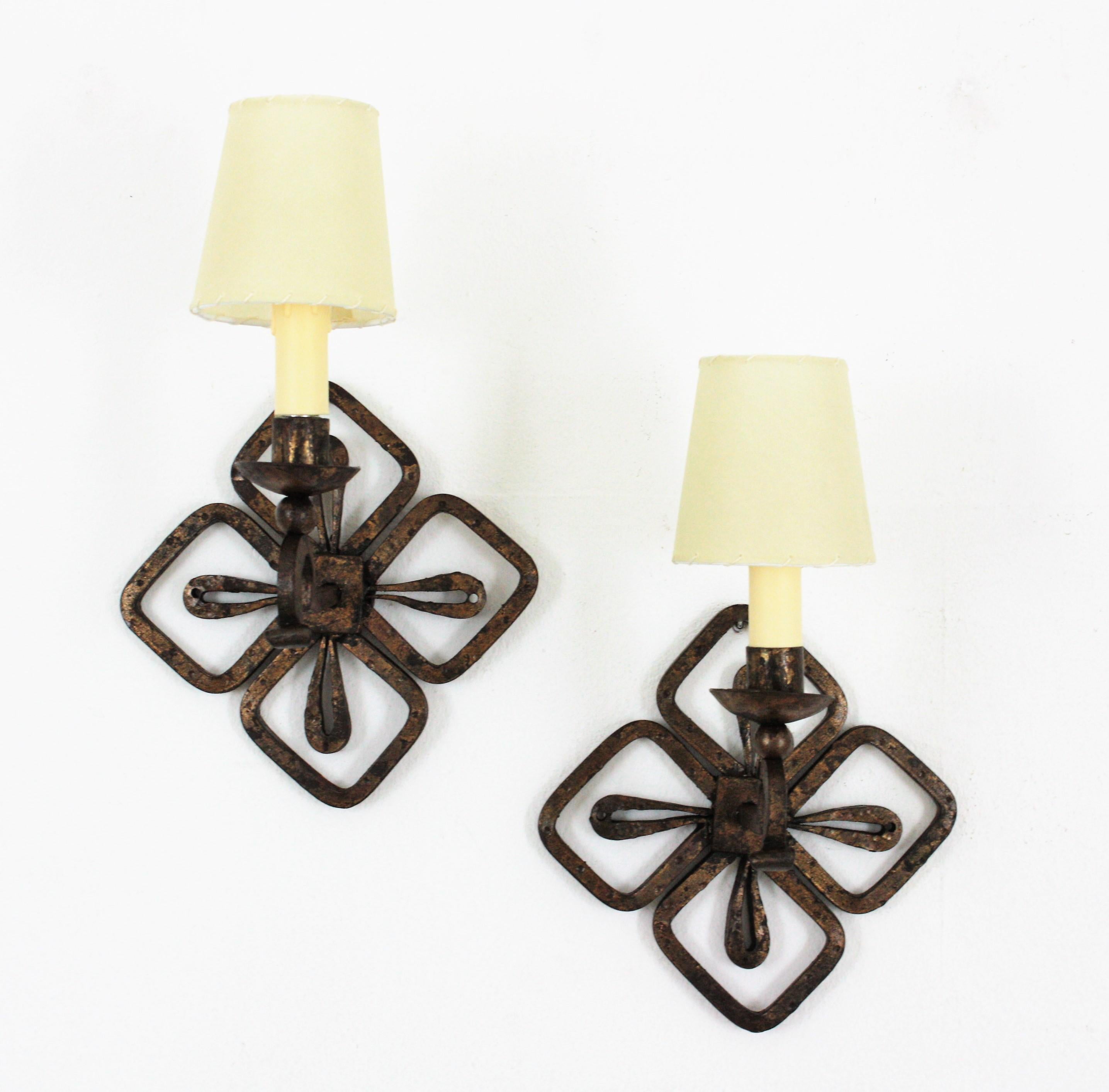 Elegant pair of wrought iron wall sconces with gold leaf gilding and Fleur de Lis Design, France, 1940s.
These hand forged light fixtures feature a fleur-de-lis shaped backplate holding an scroll ended arm with a candelabra holder with candle