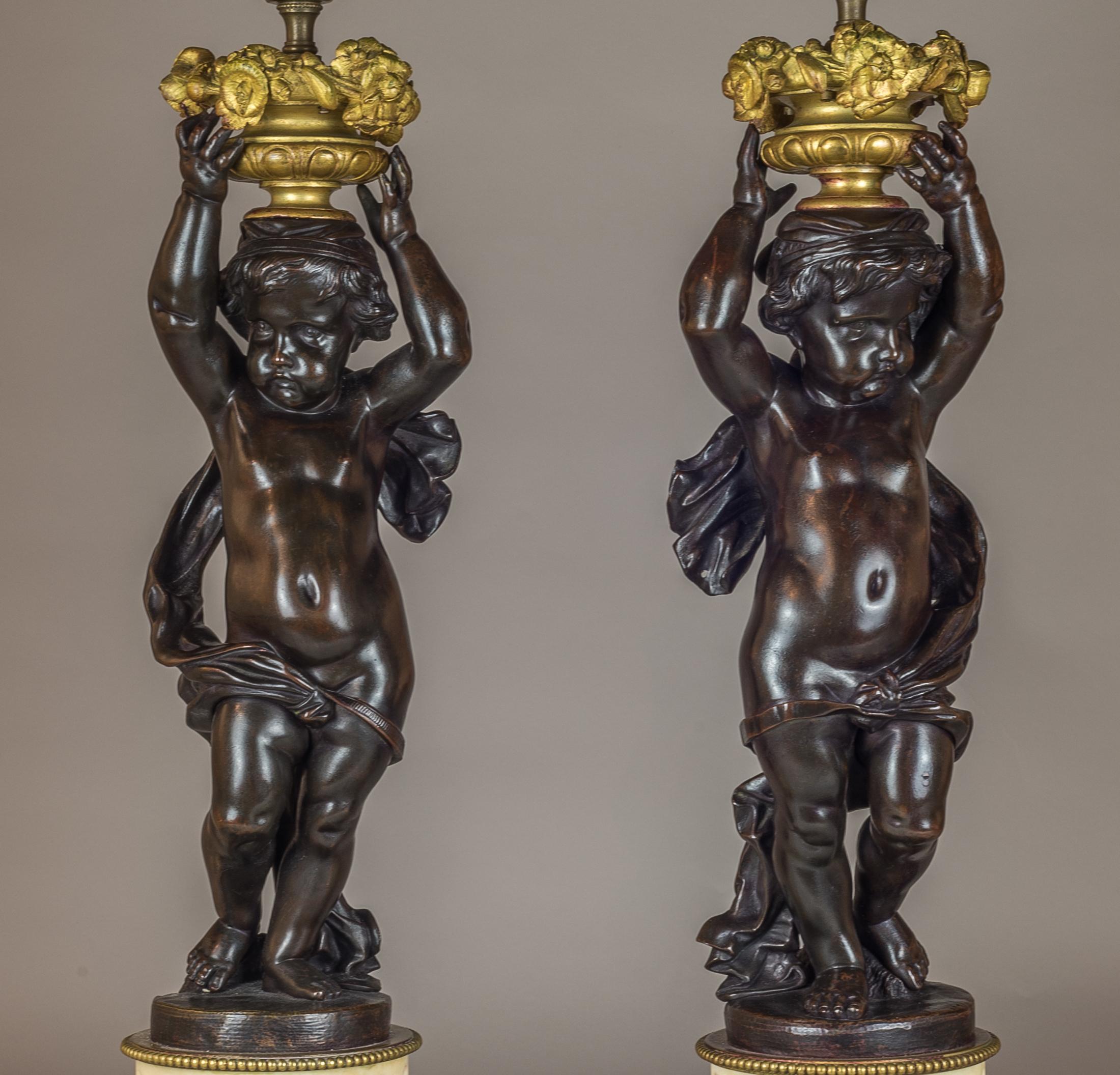 A Fine Quality Pair of French Patinated Bronze and Gilt-Metal Figural Lamps.
Each cast as a putto supporting a flower-filled urn, raised on a gilt-metal mounted white alabaster pedestal set on toupee feet. 

Origin: French
Date: 19th