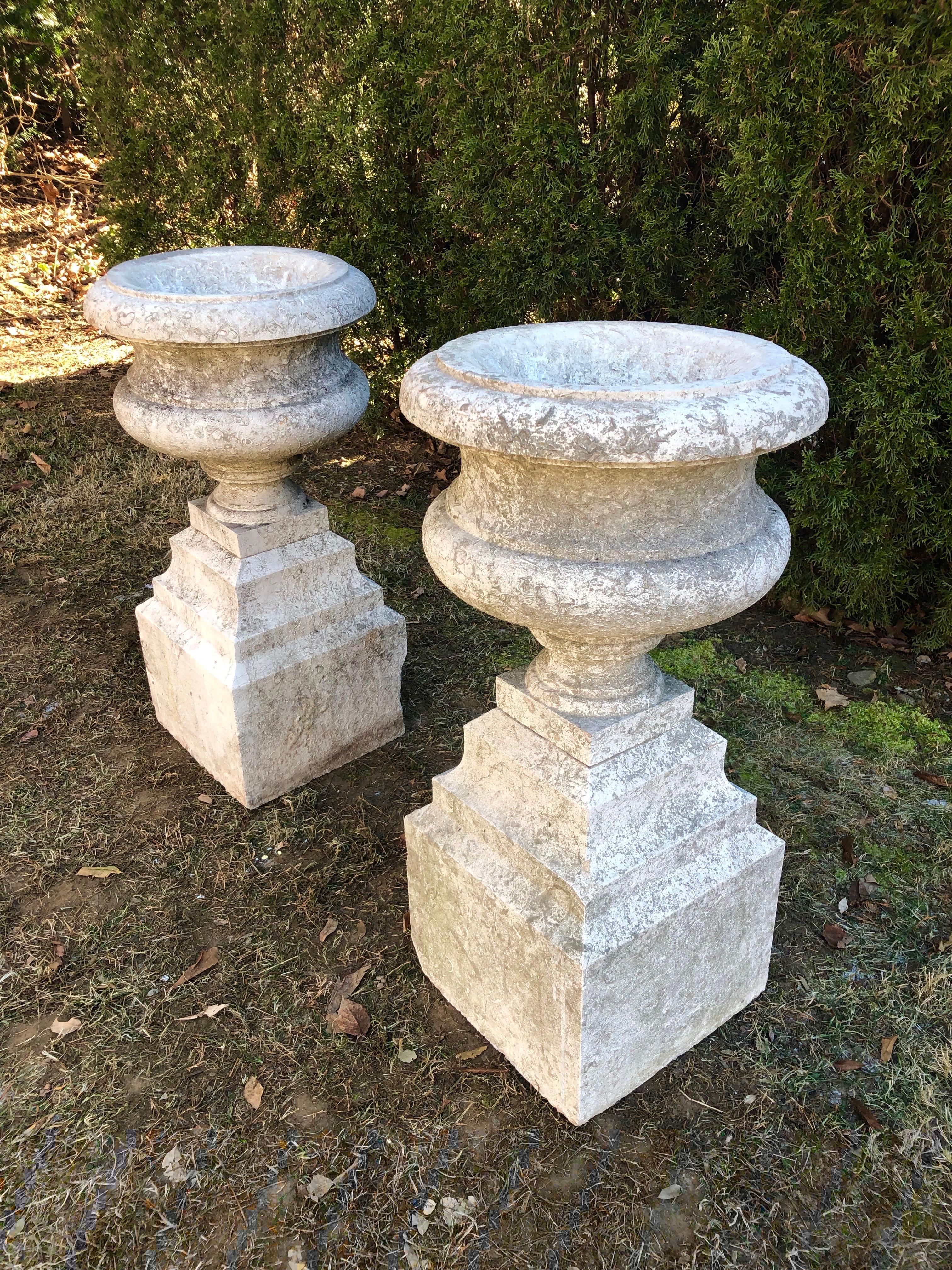 This stunning pair of urns is carved from a heavily fossilized and relatively-hard limestone quarried near Marseille, known as “Pierre de Cassis”. They feature a beautiful profile with stepped, multi-tiered bases to which the bowls are permanently