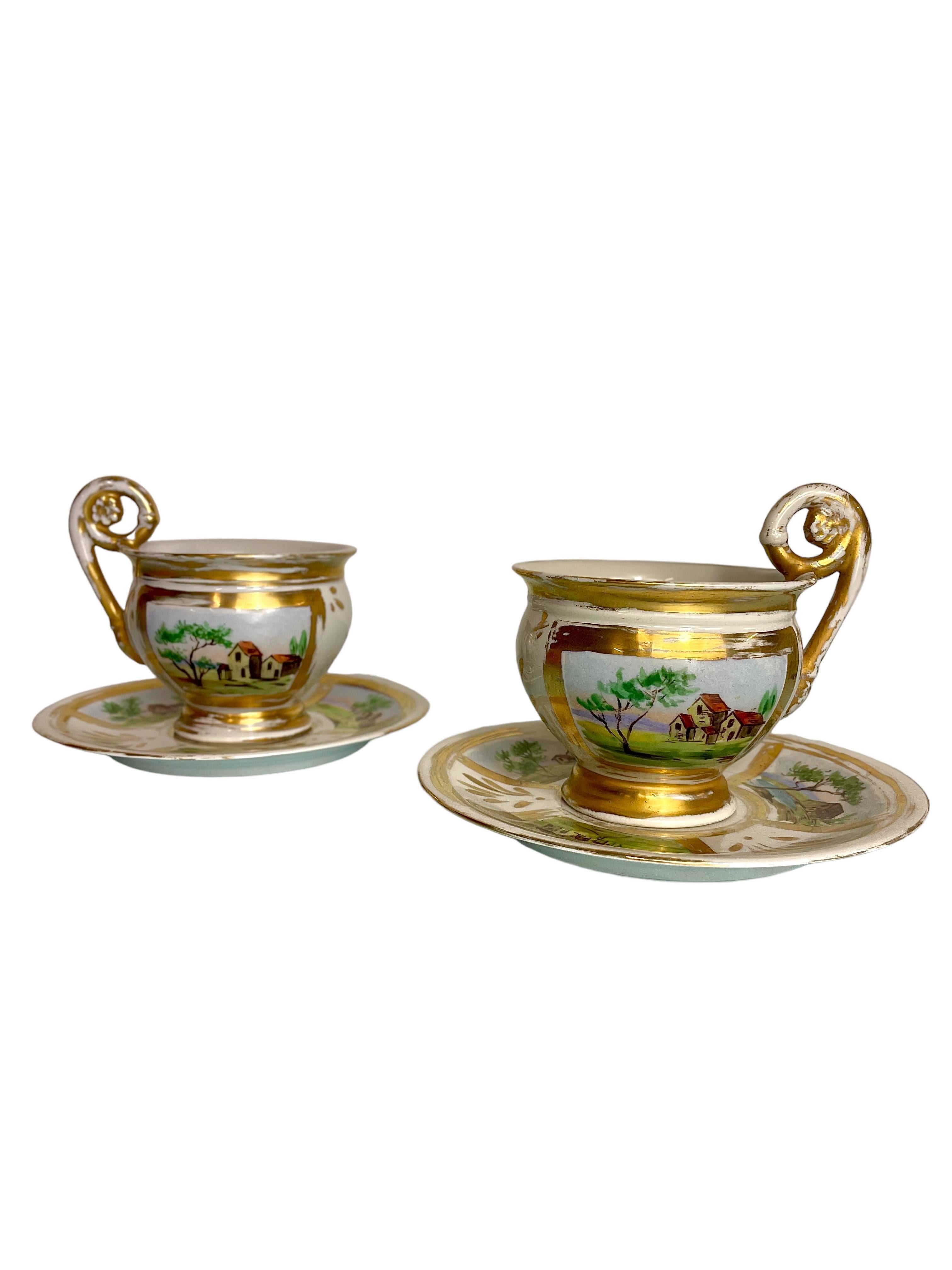 Une paire extrêmement élégante de tasses à déjeuner en porcelaine de Paris, avec les soucoupes assorties, datant du début du 19e siècle. 
Ces coupes sensationnelles sont décorées de scènes champêtres peintes à la main et rehaussées de généreuses