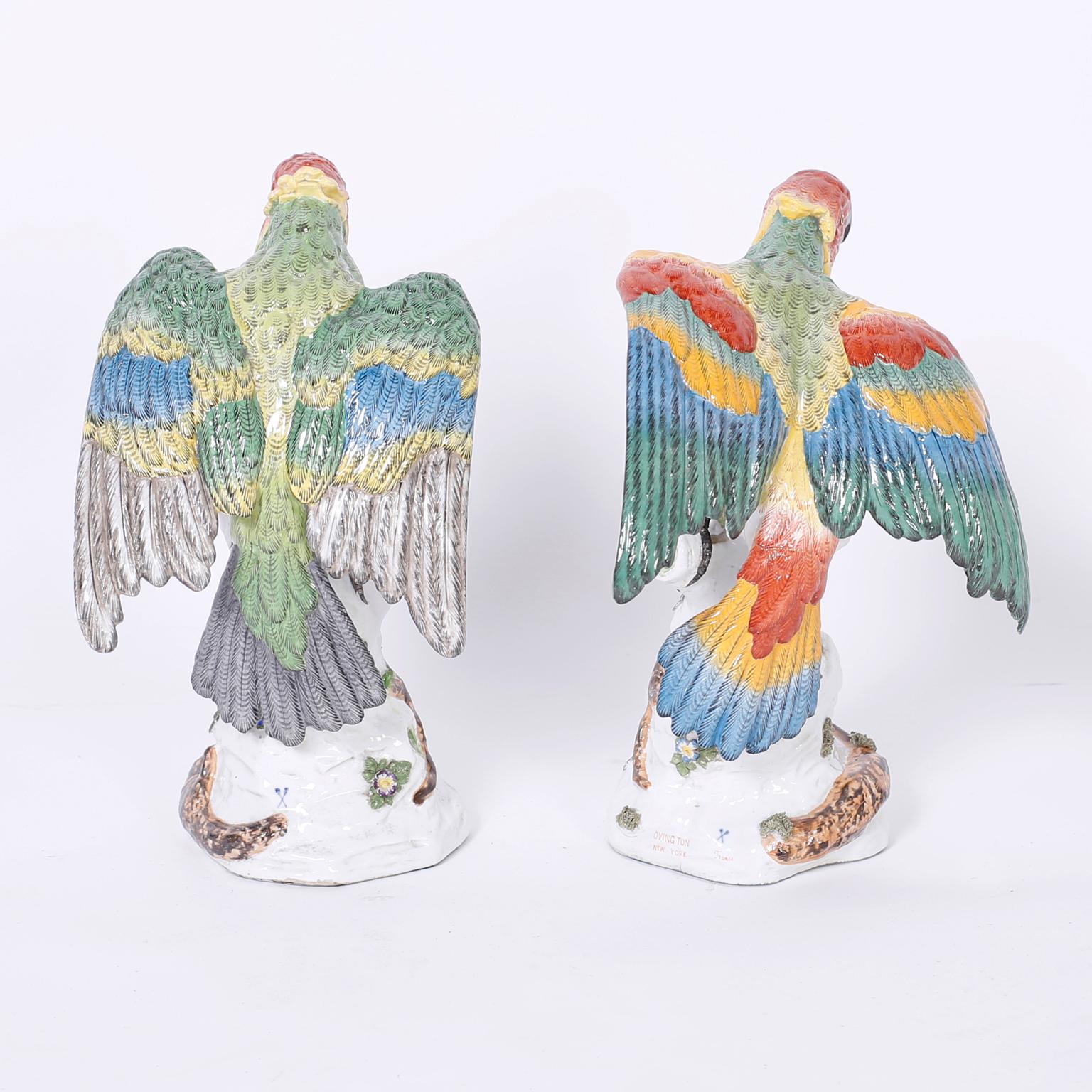 Pair of French porcelain parrots with lively expressions and colorful plumage perched on tree trunks with flowers. Originally sold by noted importers Ovington New York.