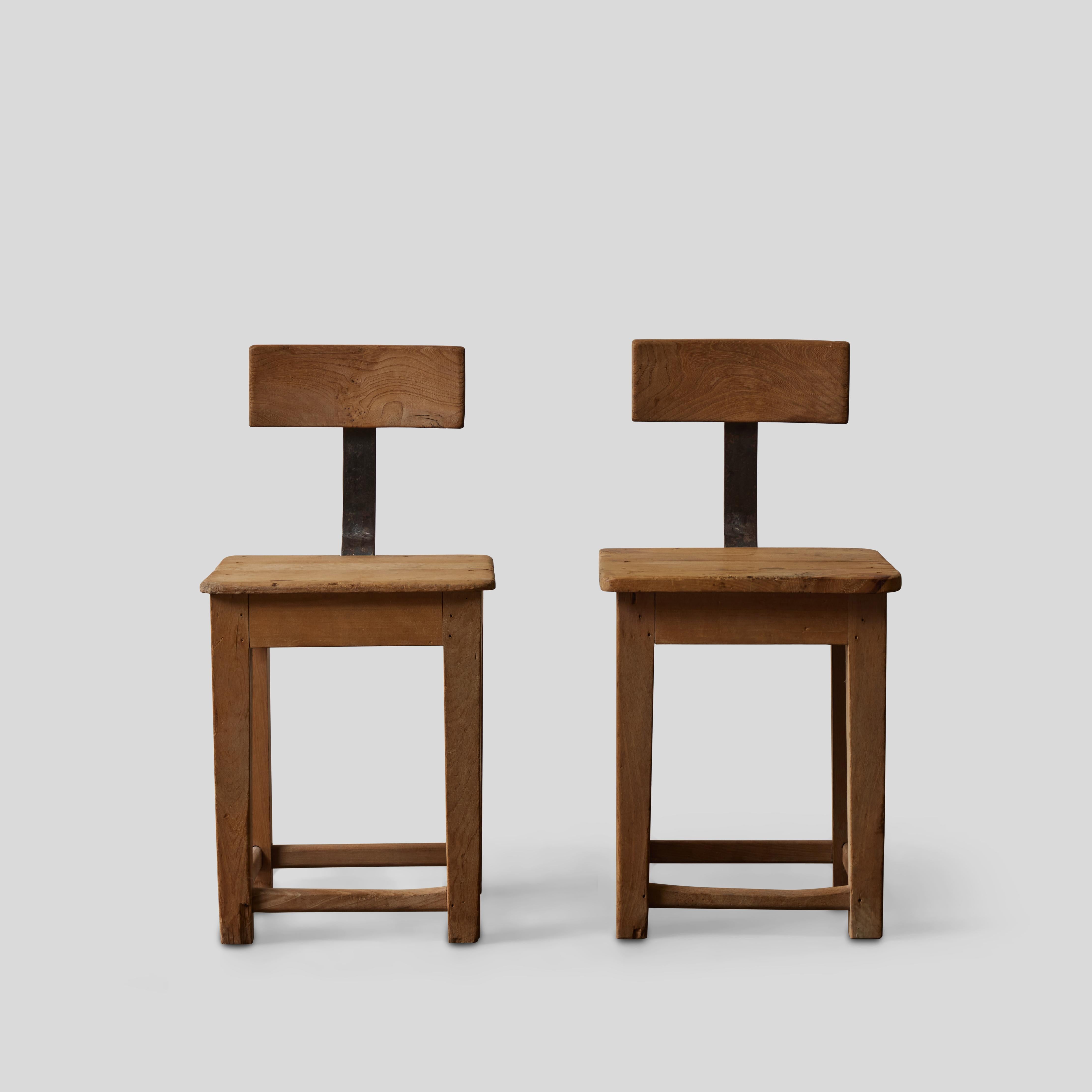 Pair of early 20th-century French Primitivist wood dining or side chairs with industrial metal accents. The wood has a raw finish, which complements the chairs' stark geometric design. Time and wear has developed a unique rustic patina and finish