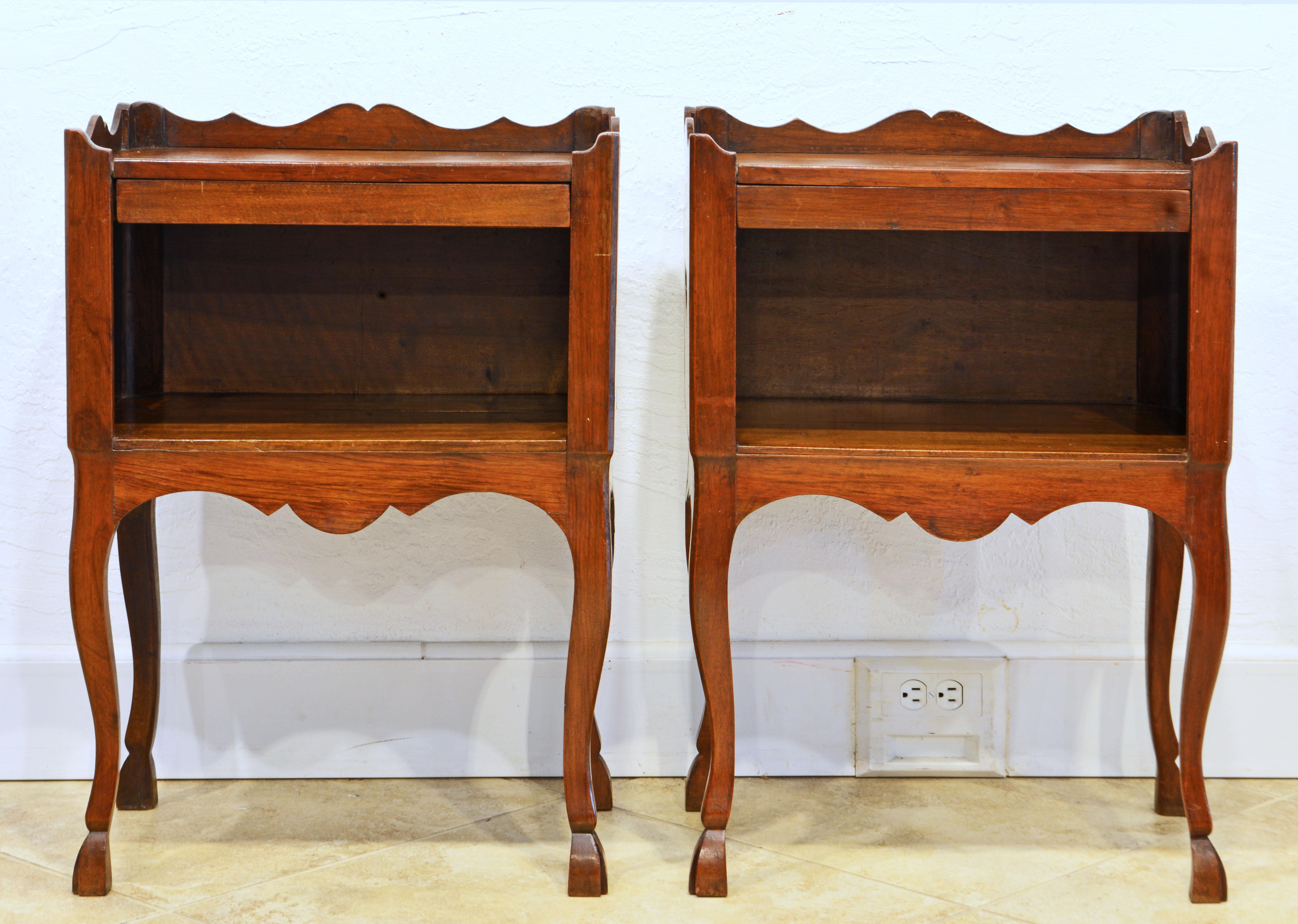 Dating to the mid 19th century this charming pair of French Provincial side tables or commodes feature beautifully carved scalloped galleries surrounding the three sides and shallow concealed drawers above open compartments lit by heart shaped