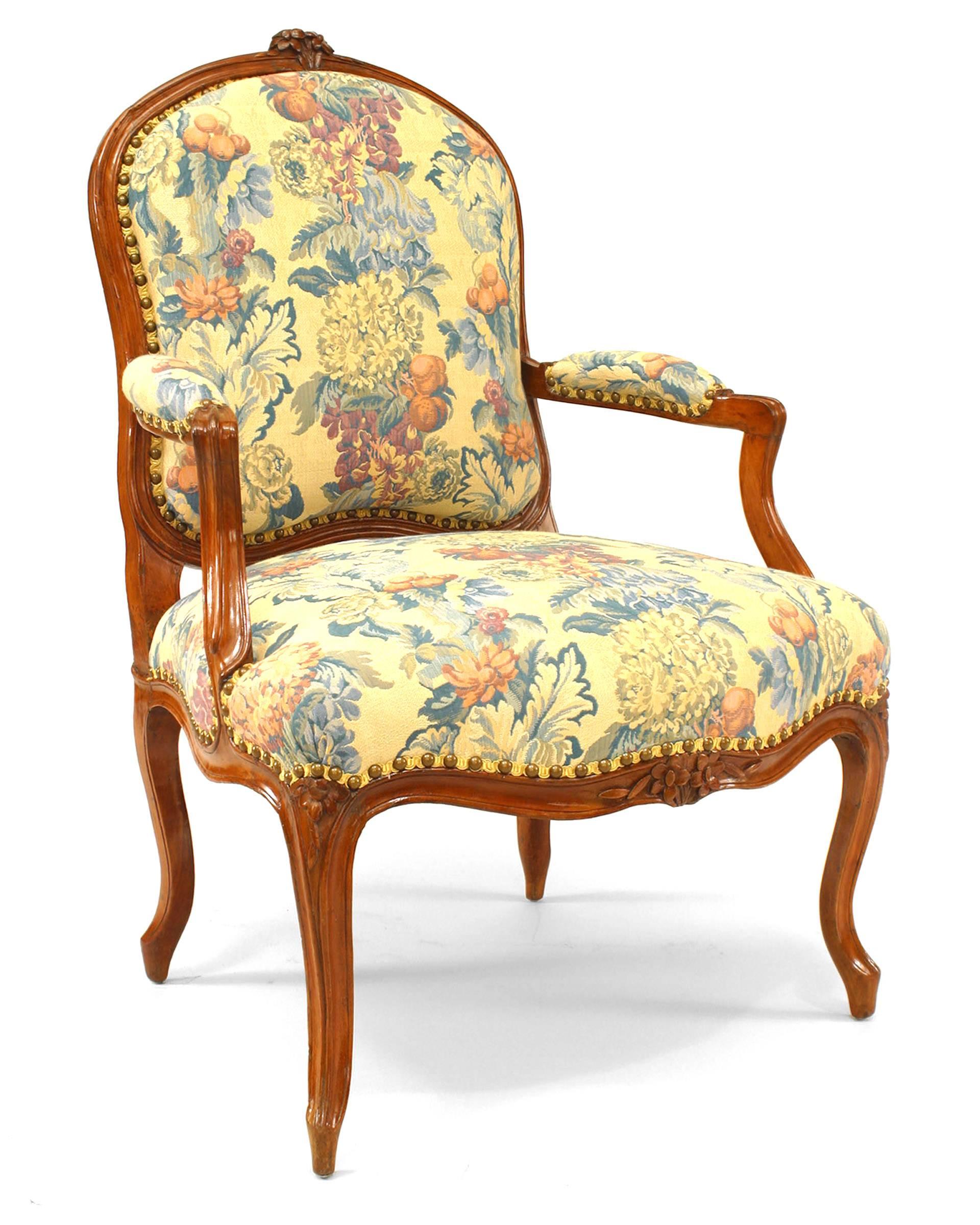 Pair of French Provincial Louis XV open Armchairs with carved floral crest on top of back frame with floral upholstered seat, back and arm rests
