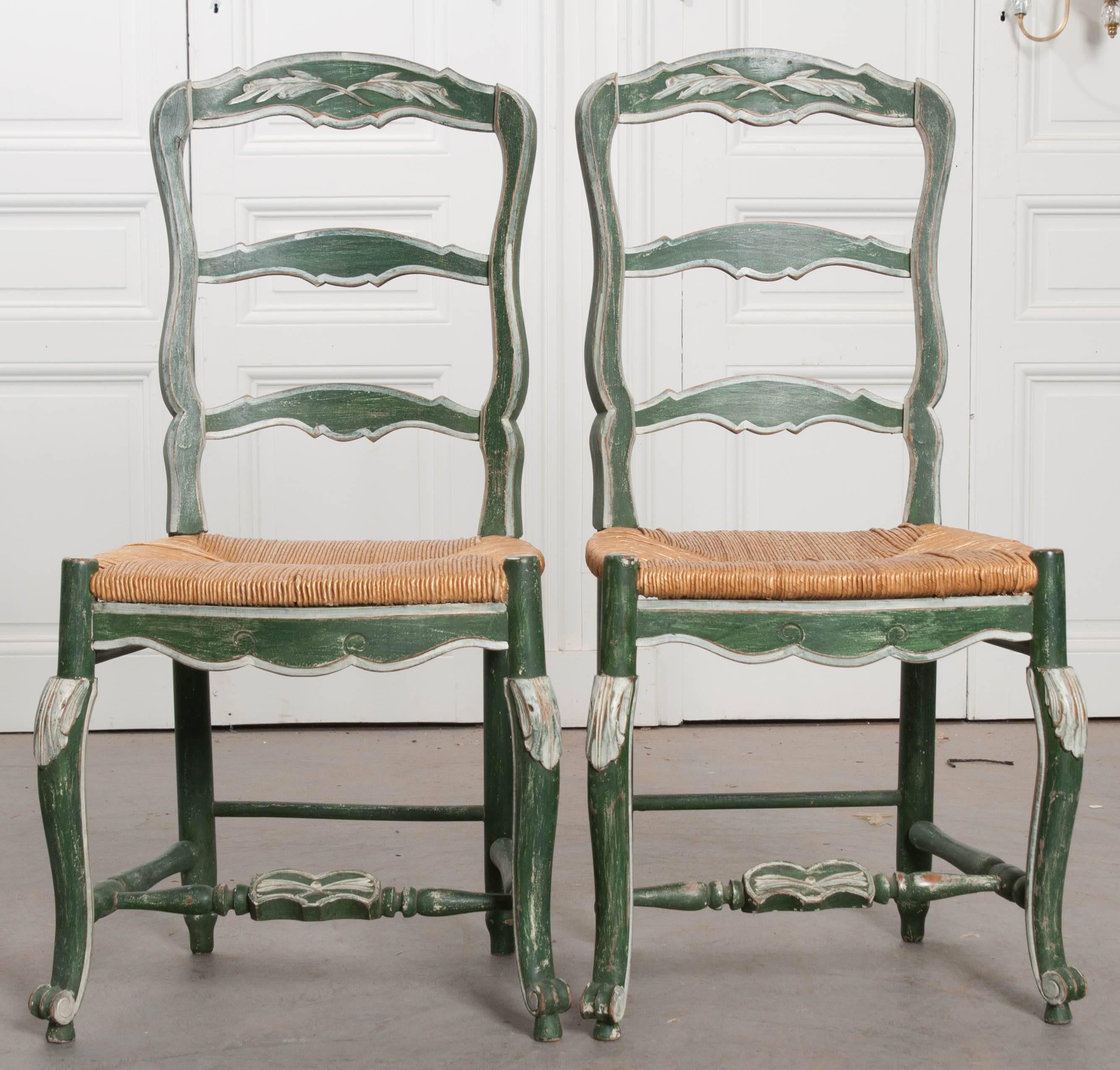 A pair of early 20th century Provincial rush seat ladder back dining chairs. The chairs have been recently painted green, with soft white trim. The finish is antiqued. The rush seats are in good antique condition, and have a height of 17 1/4?.