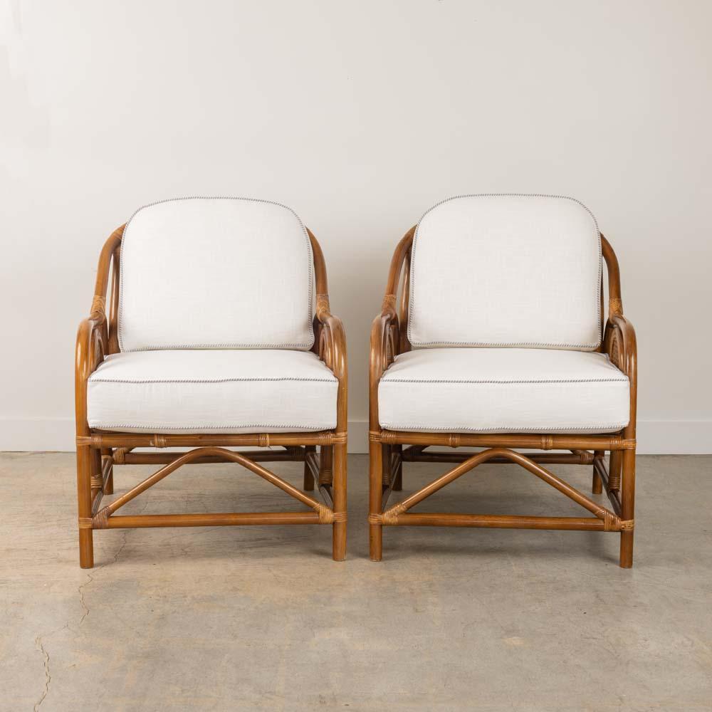 Wonderful pair of 1950's French rattan and cane chairs with cushions. Curved slatted rattan frames with wrapped rattan detail and unique circular cane detail on sides. New off-white linen cushions with great blue and white striped trim. Rattan