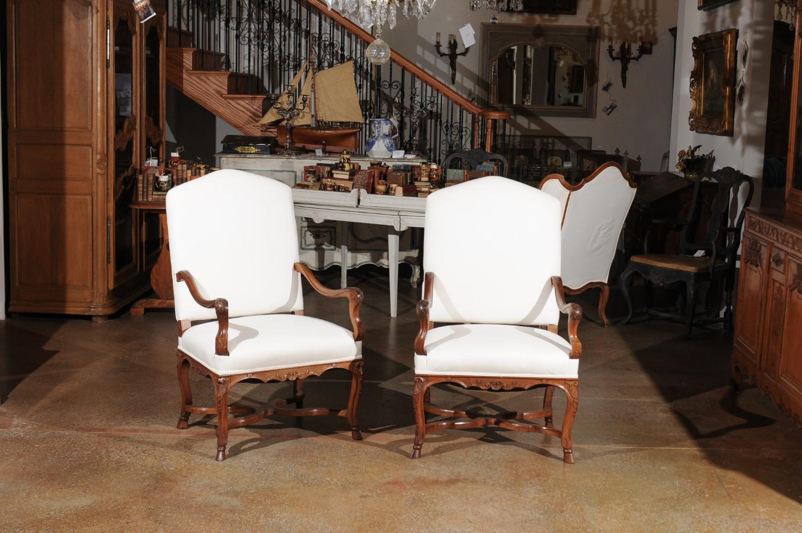 A French Régence style walnut armchair from the late 19th century, with new upholstery, cabriole legs and X-form cross stretcher. Born in France during the later years of the 19th century, each of this pair of armchairs features a slightly slanted