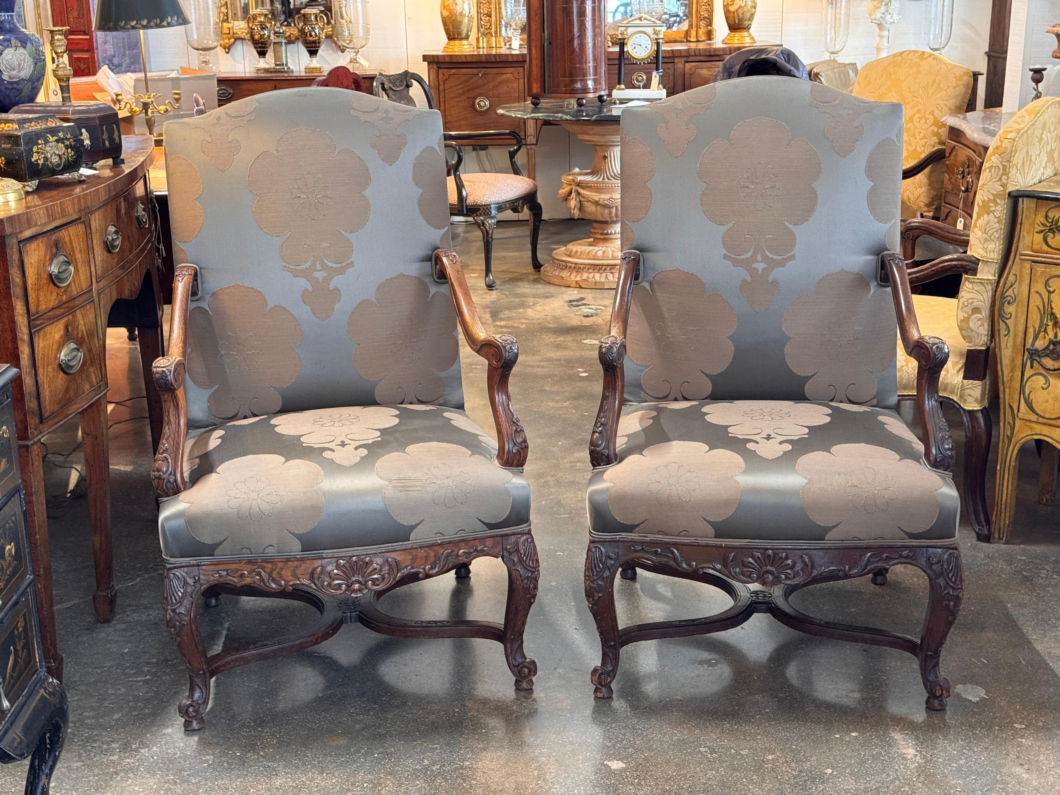 Pair of walnut armchairs carved with scrolling accents along the arms and apron, shown clearly in the detail image. The shaped backs and cabriole legs are consistent with Regence-style forms, and both chairs are upholstered in a patterned fabric