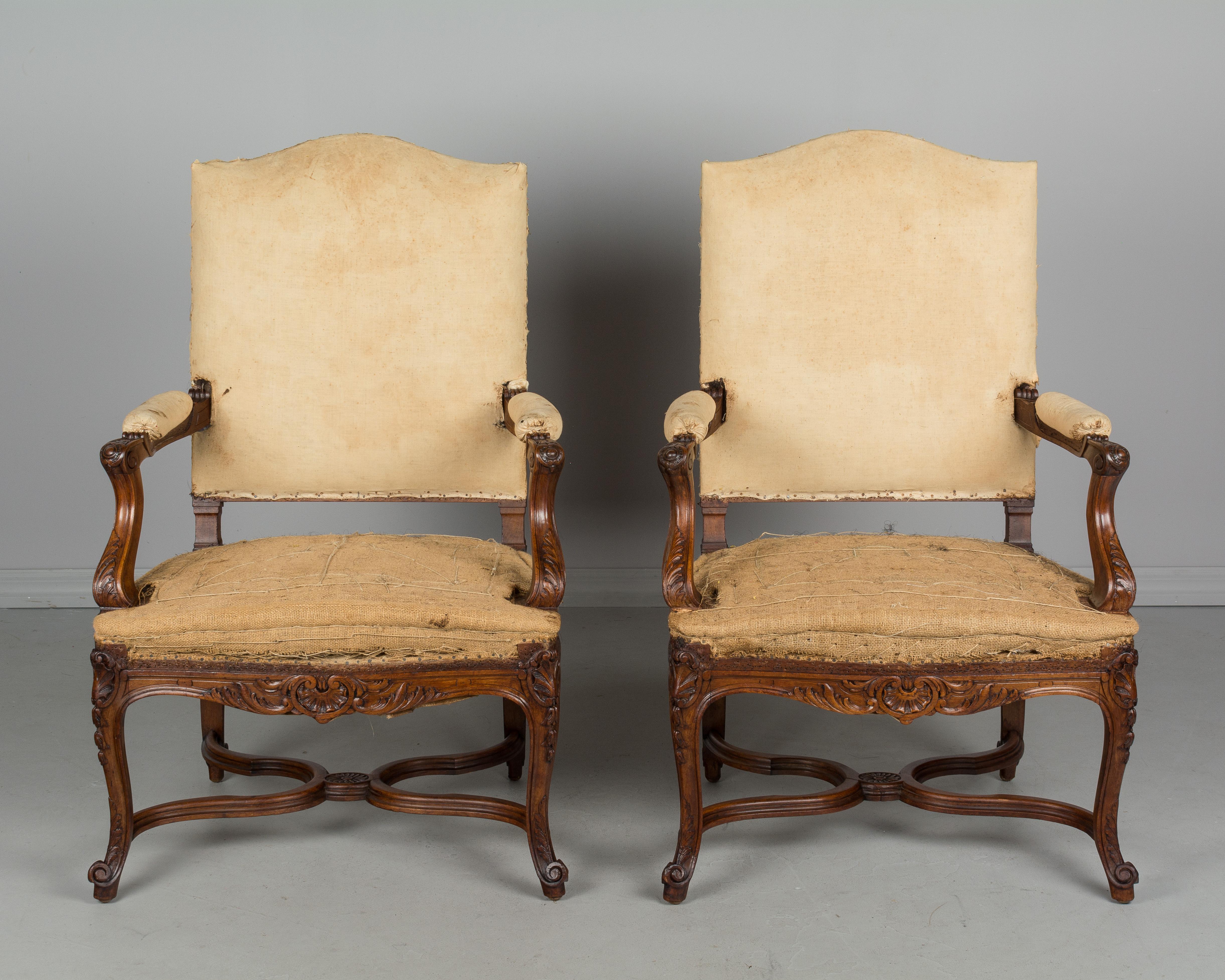 Pair of French Regence style fauteuils, or arm chairs. Hand-carved walnut frames with X-stretcher. Sturdy with comfortable proportions. Stripped of old fabric and sold as is. Another pair is available. Check our listings. Please refer to photos for