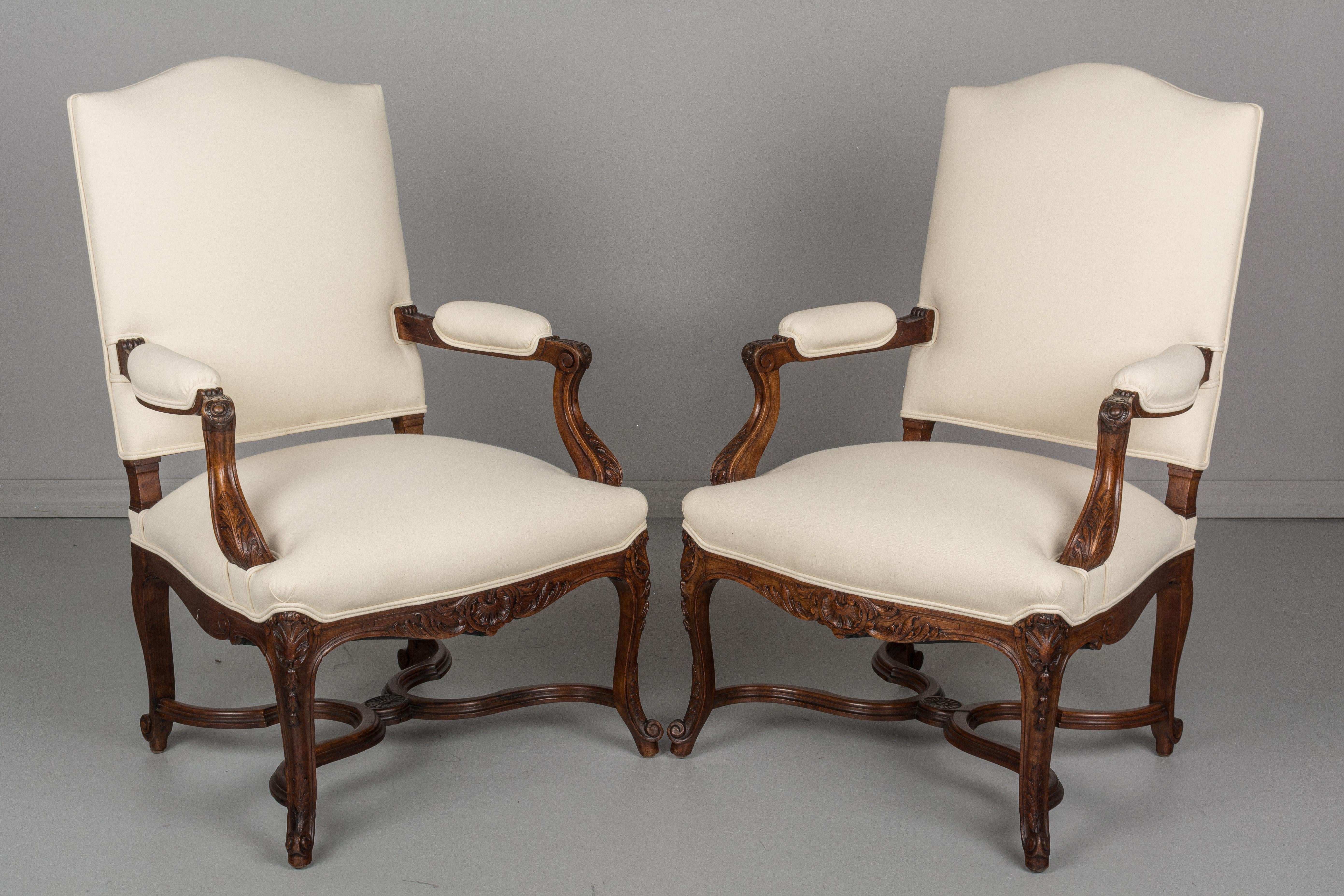 A pair French Regency style fauteuils, or arm chairs with hand carved walnut frames and X-stretcher. Sturdy with comfortable proportions. Upholstered in a new natural cotton canvas fabric. Please refer to photos for more details. We have a large