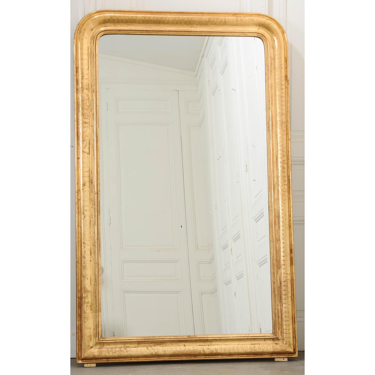 A fine pair of large gold giltwood mirrors from 20th century France. These mirrors are reproductions of the highest quality and embody the Louis Philippe style entirely. The linear frame has its signature curved top corners and brilliant gold gilt