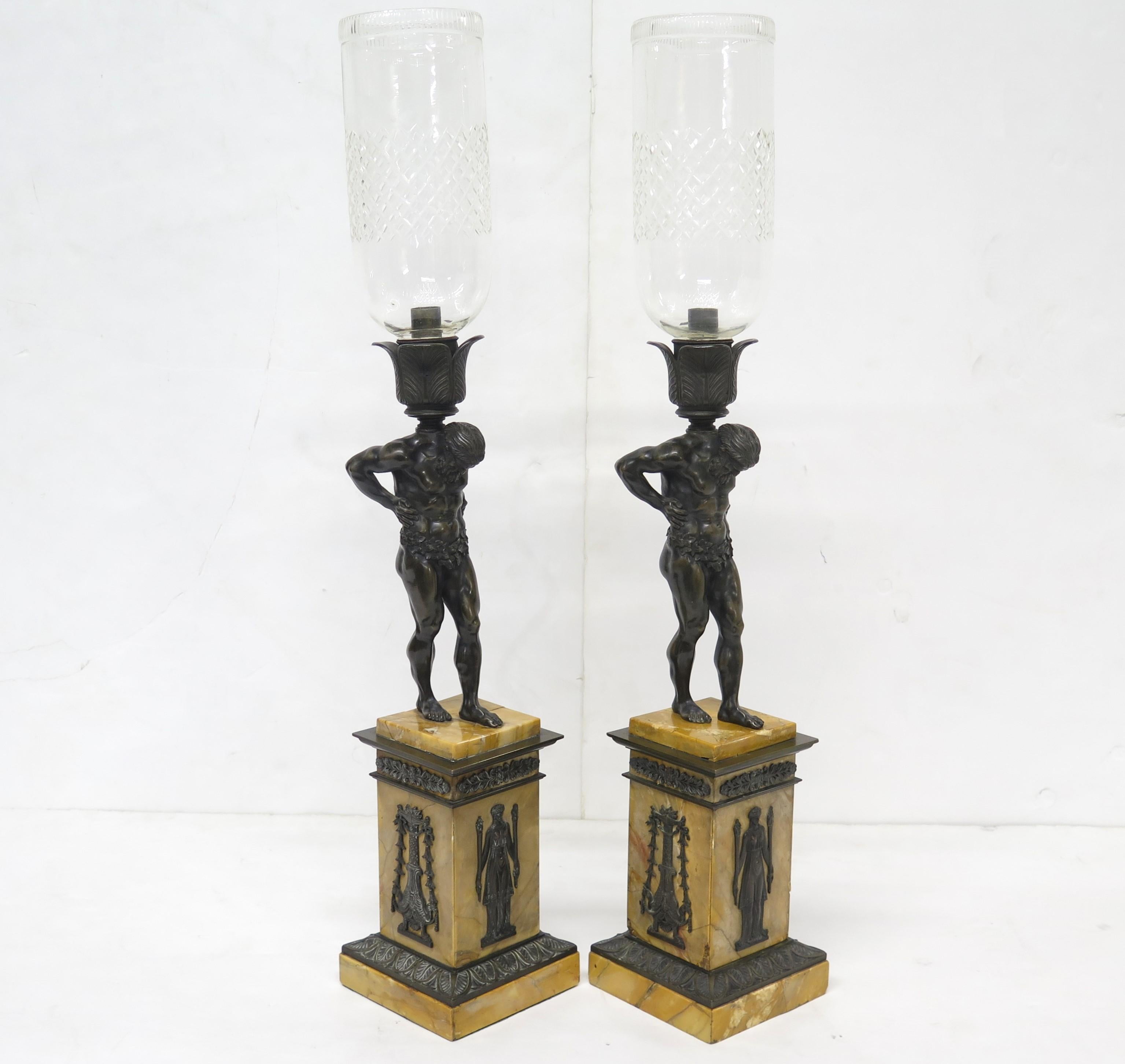 Pair of French restoration period candlesticks of patinated bronze and gilt bronze with figures of Atlas supporting a flower bobeche and etched glass hurricane. The bases are in sienna yellow marble. France. Early 19th Century.