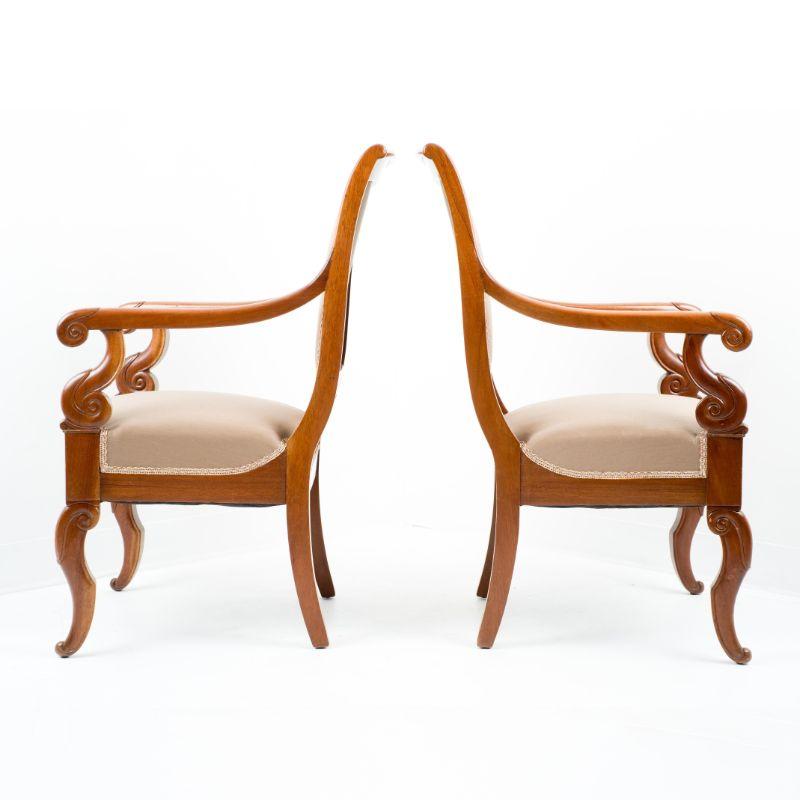 Pair of French Restoration mahogany frame upholstered fauteuils. The square back frames support an upholstered panel, and the upholstered seat is framed by mahogany rails on four carved mahogany legs. The arms thrust forward from the upper back