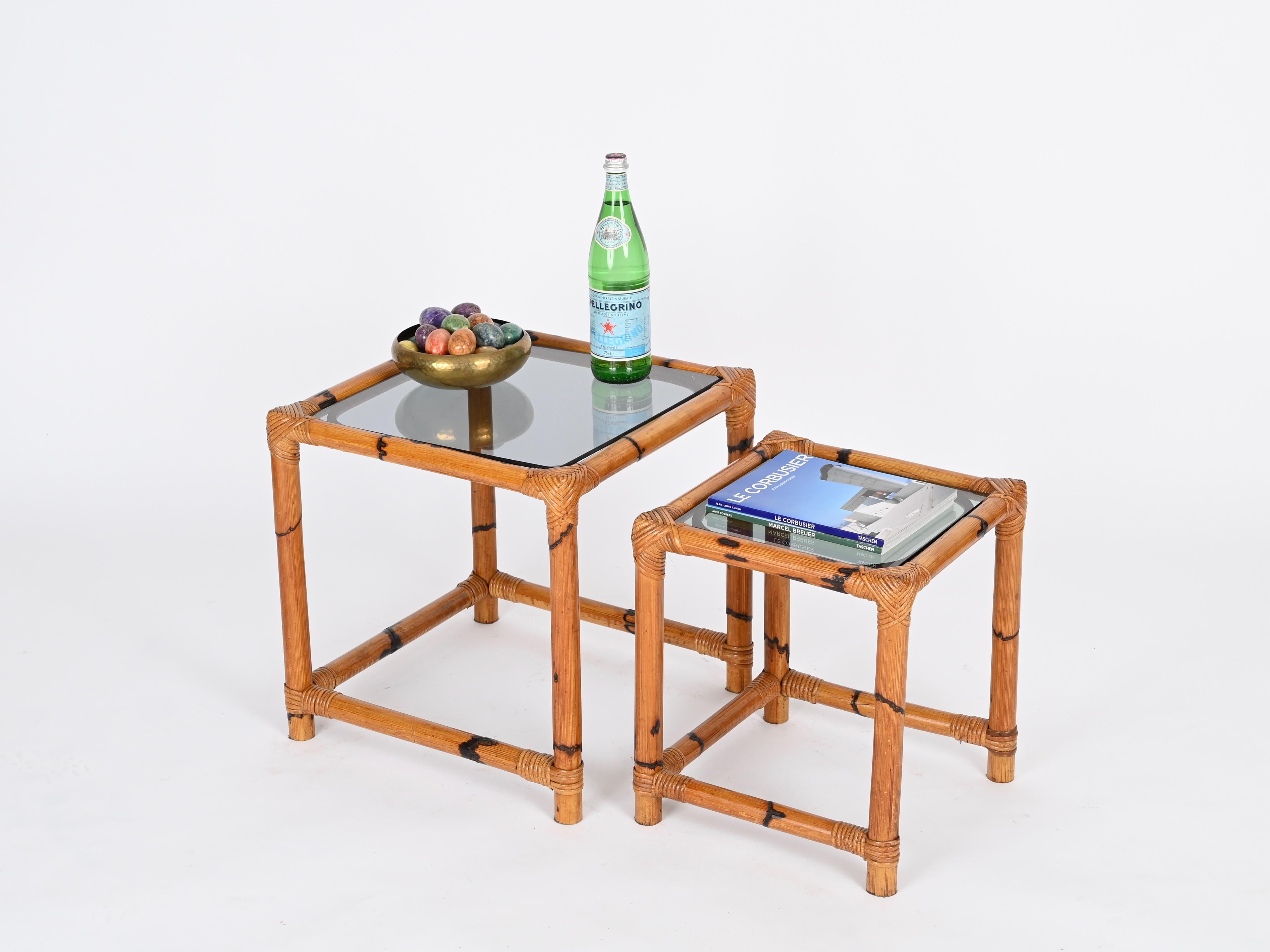 Gorgeous pair of French Riviera style nesting tables in bamboo and hand-woven wicker with smoked glasses. This marvelous organic tables were designed in Italy during the 1970s.

In fabulous condition, these square tables have a charming and vibrant