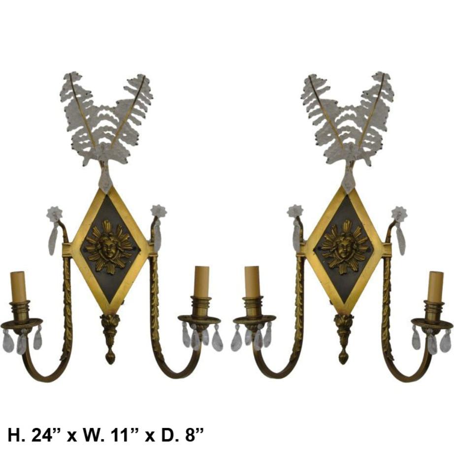 Lovely pair of French neoclassical style rock crystal and gilt bronze two light sconces. (A)
Each sconce is surmounted with two crystal beaded leaves, above a gilt bronze and patinated diamond shaped back plate with a central panel depicting a