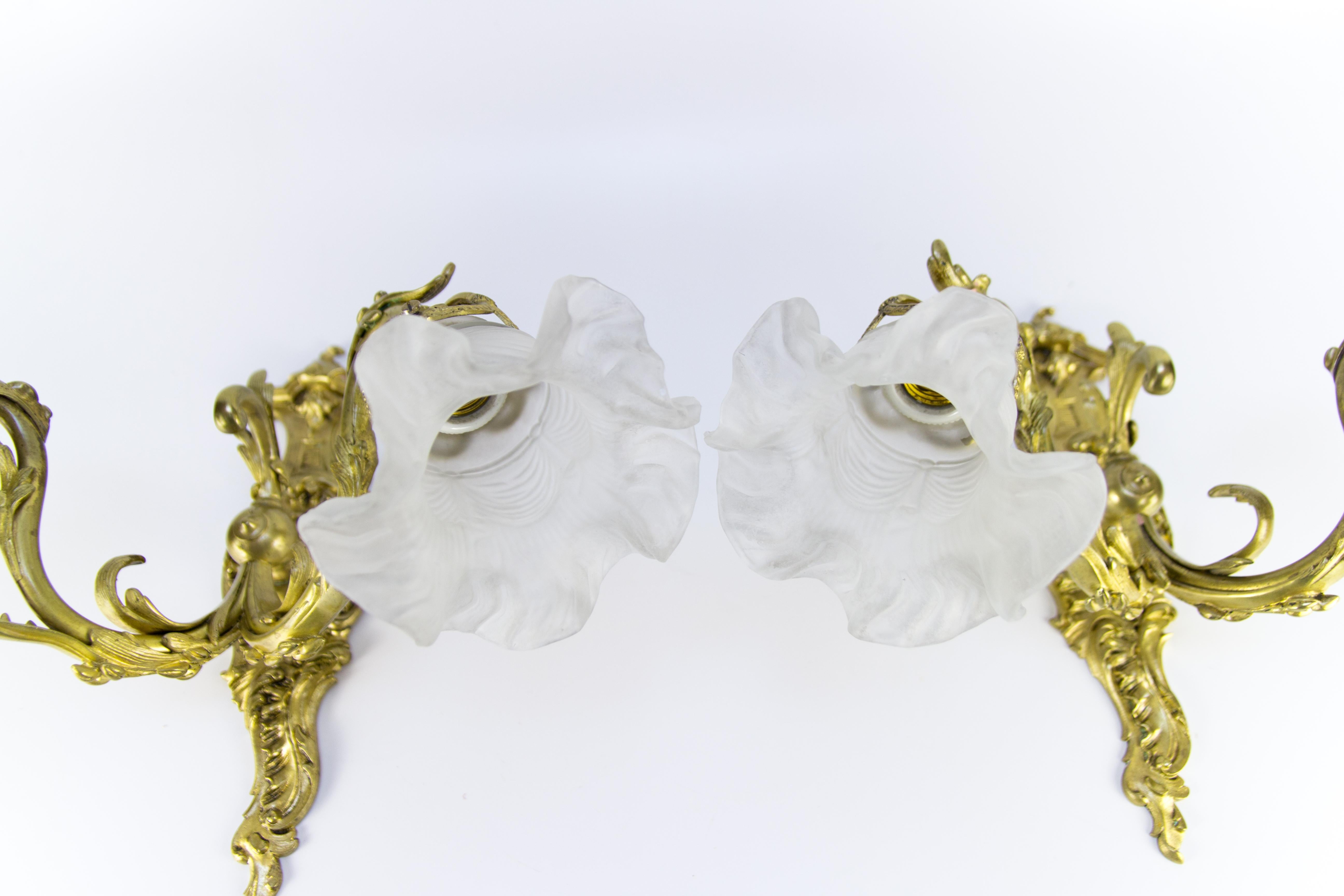 Zwei französische Bronzewandleuchter im Rokokostil aus den 1920er Jahren. Schöne verschnörkelte Rokoko-Details. Jede Leuchte hat zwei Arme aus Bronze und Schirme aus mattiertem Glas, jeweils mit Glühbirnenfassungen der Größe E27 (E26).
Maße: Höhe 35