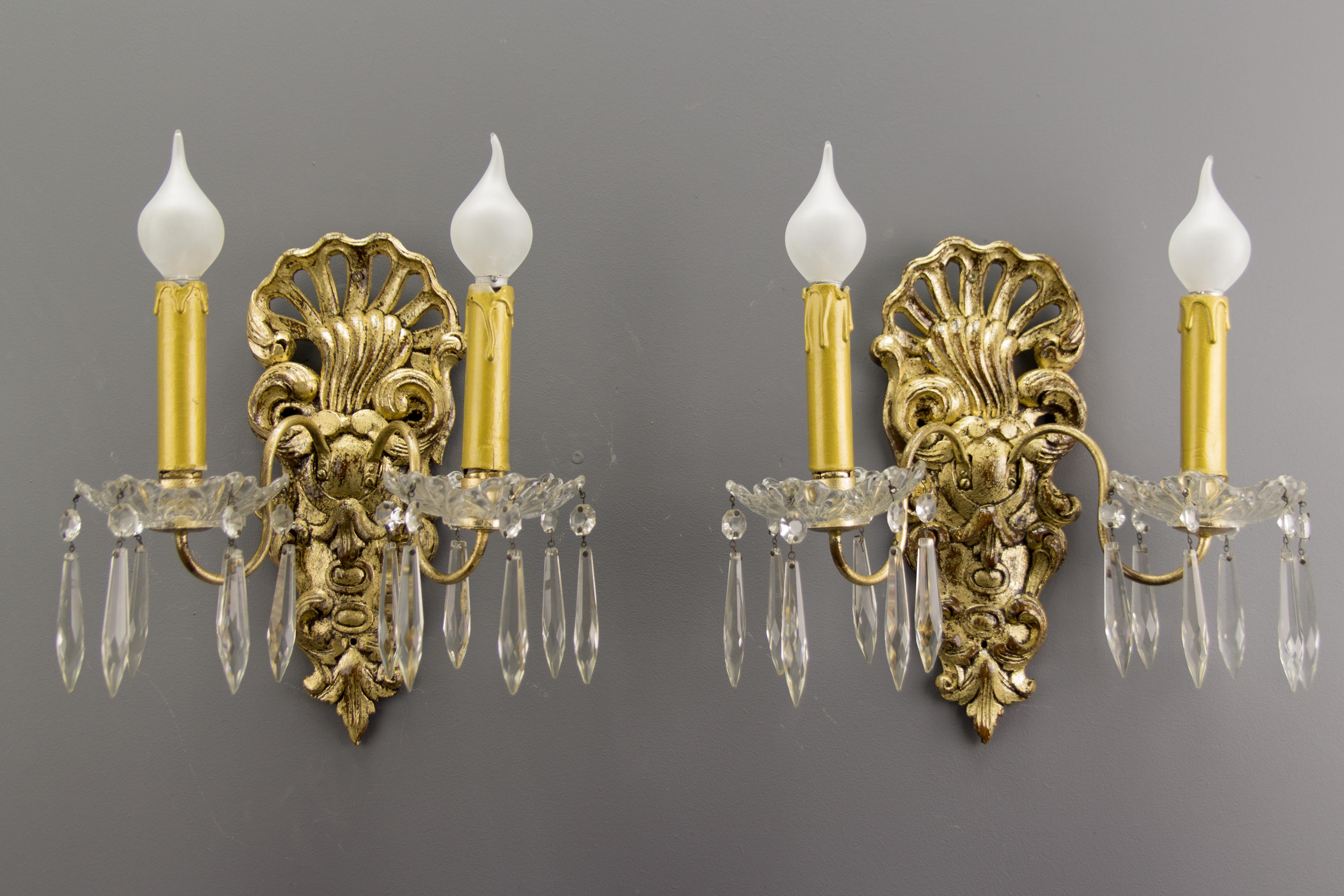 A pair of French Rococo-style carved wood sconces from the early 20th century. Sconces are electrified and ornate with pending crystal glass droplets.
Each sconce has two brass arms and each arm has one socket for an E14 size light bulb.