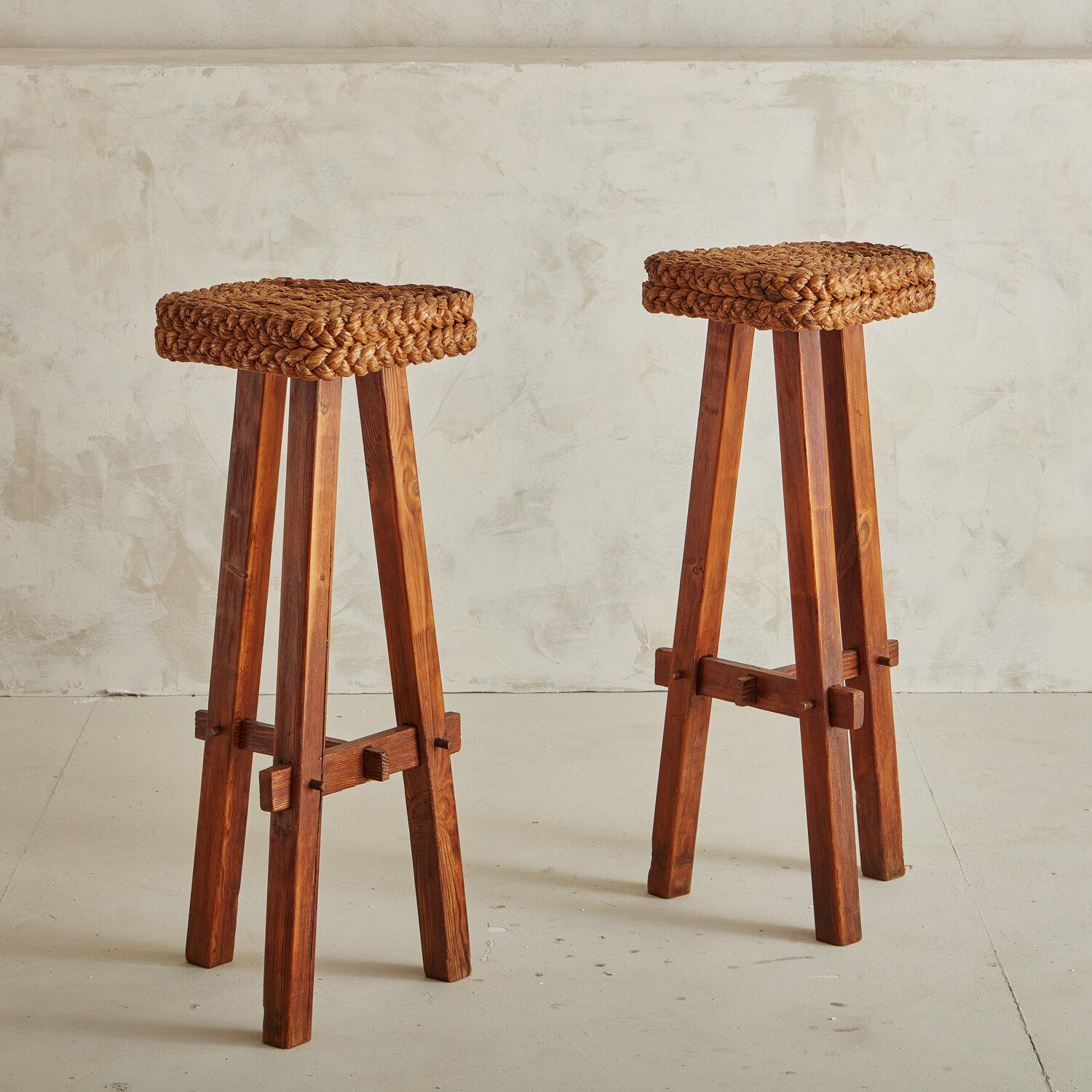 A pair of handsome French 1950s bar stools attributed to and in the likeness of design team, Audoux & Minet. Sourced in France. The seats feature woven abaca rope cord with a tripod stained beech wood base. 

Audoux and Minet became known for