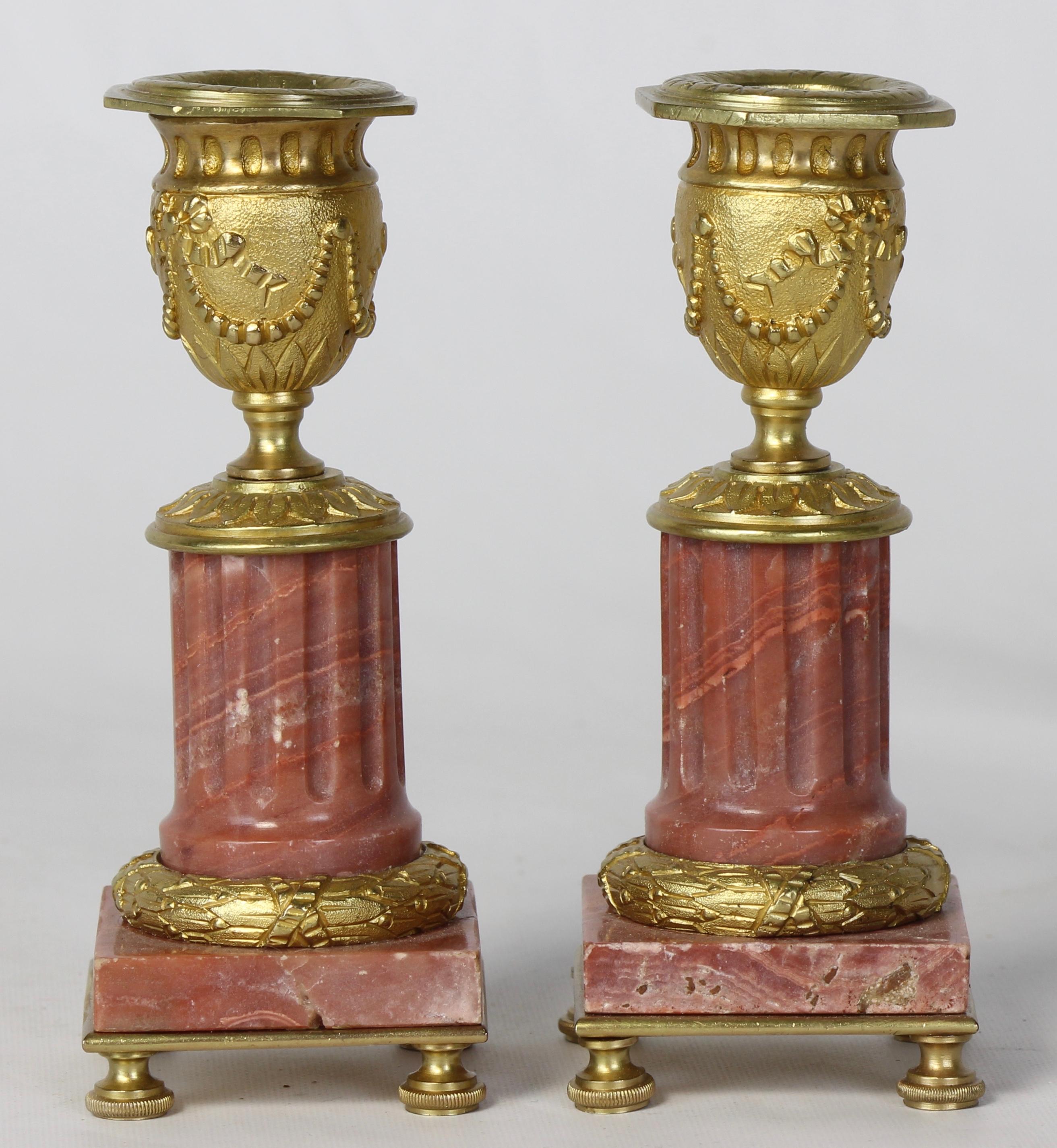 A pair of early 20th century French small scale gilt bronze and rose marble neoclassical style candlesticks in the form of fluted columns supporting classical urns.