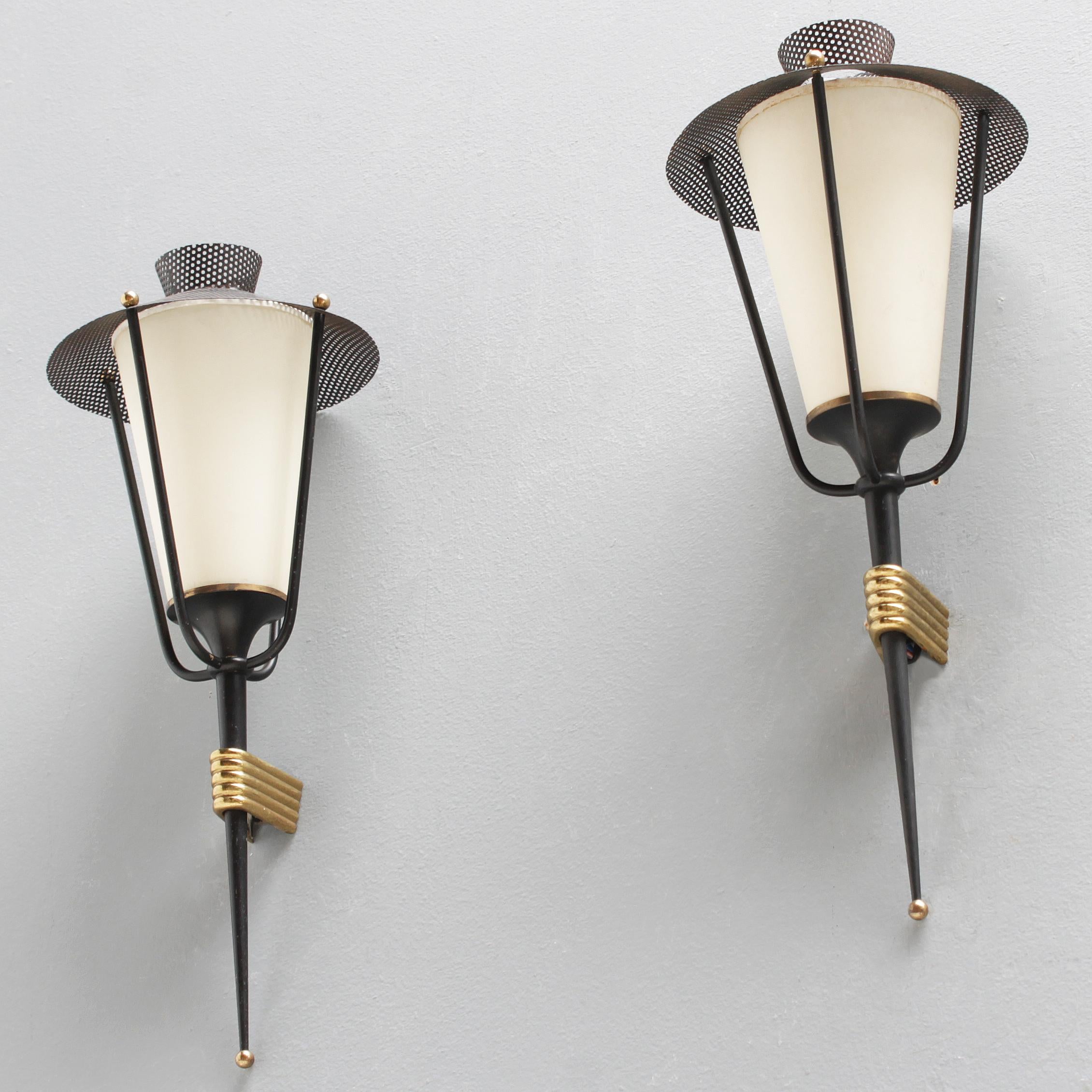 A pair of beautifully elegant black wall laterns by Maison Arlus France. 1950-55. Perforated black metal with brass details.
Fully original, unrestored. In a very good condition. Often the shades are damaged or they have much too white restored