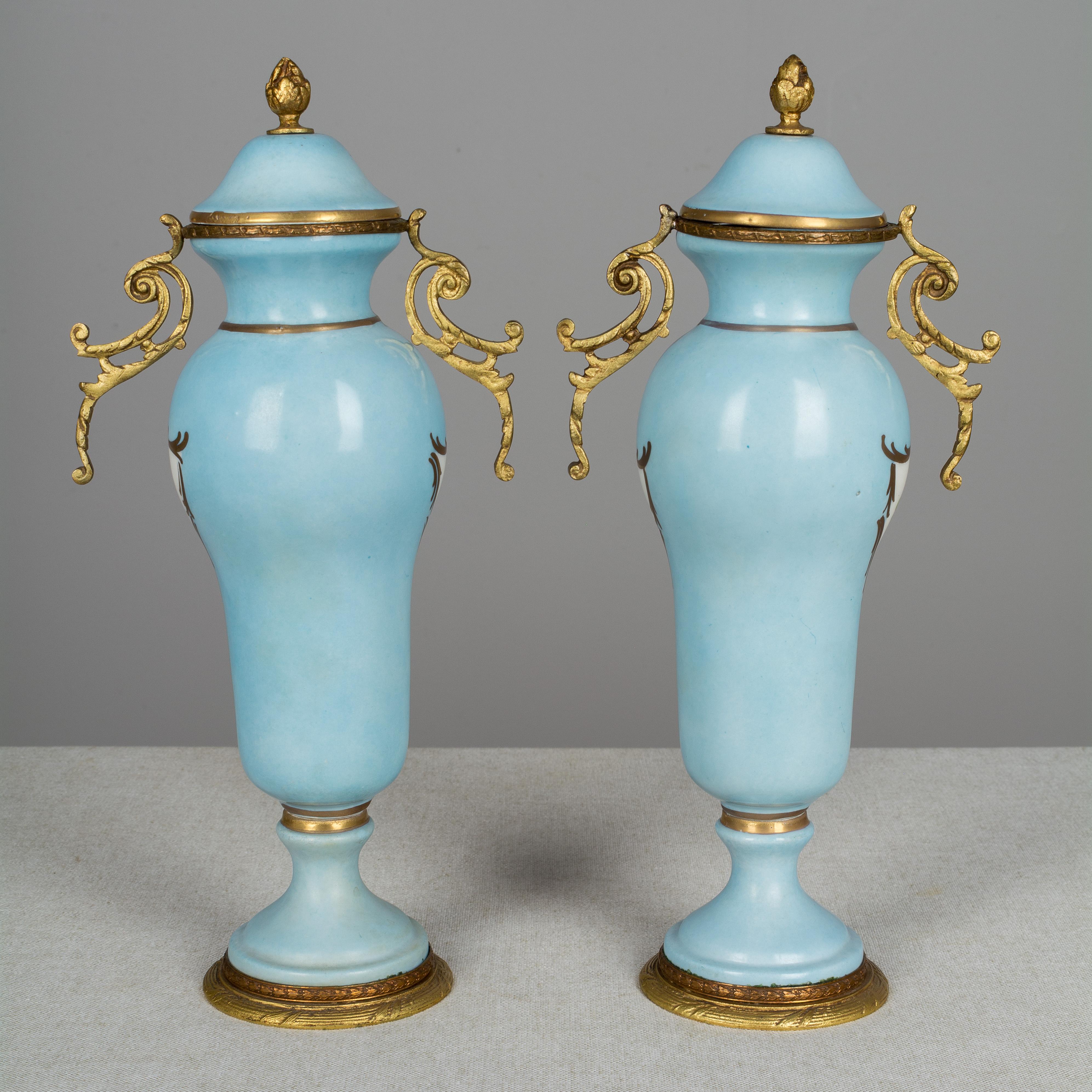 A pair of 19th century French Sèvres Porcelain bronze mounted urns, each with pastoral scenes on blue ground with hand painted gold accents. Marked on bottom.