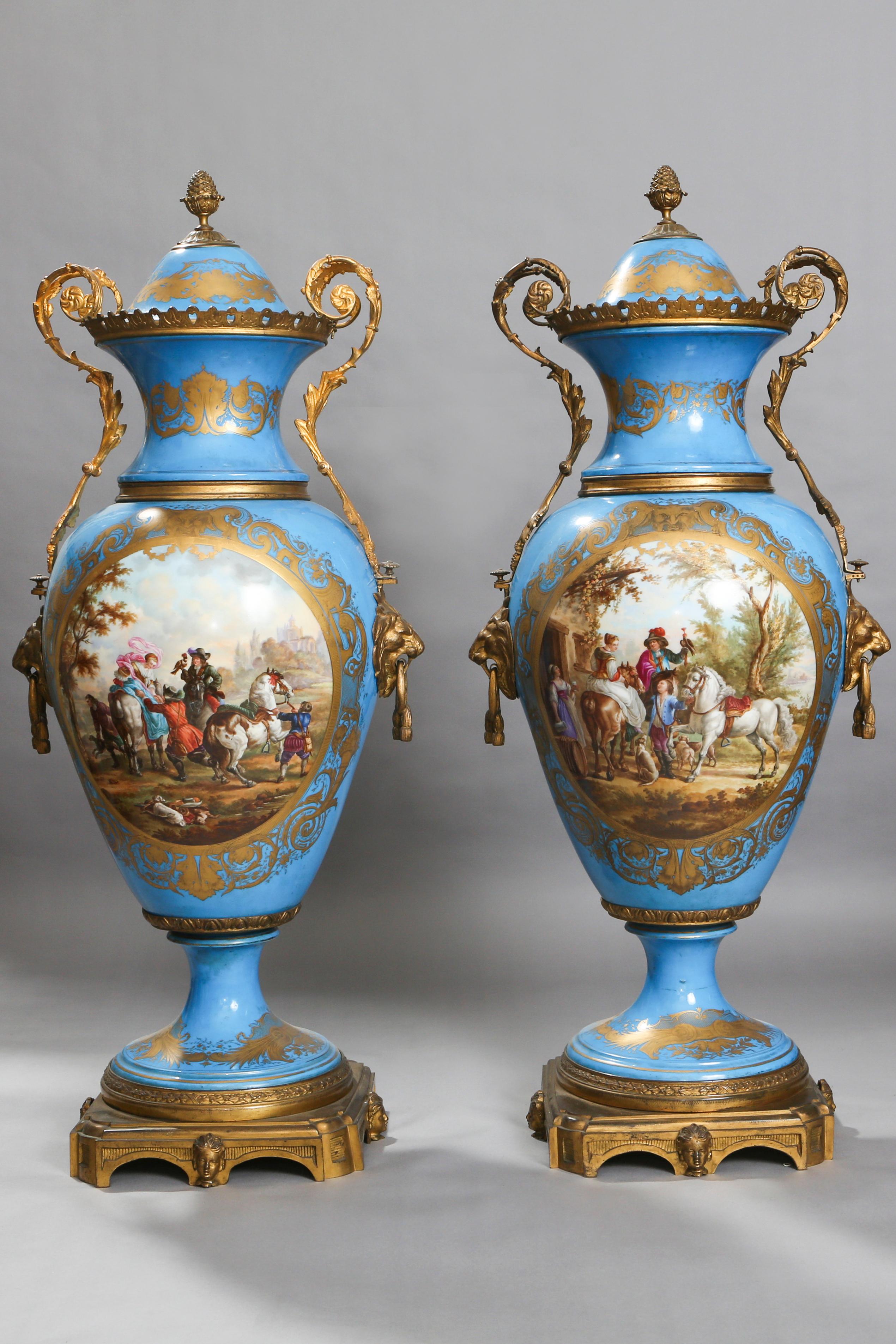 These Classic, light blue background, porcelain vases stand tall on a golden carved octagonal pedestal. Each base is decorated with beautiful gold scrolls and leaves. The painted panel to the front of the vase depicts a 19th century French village