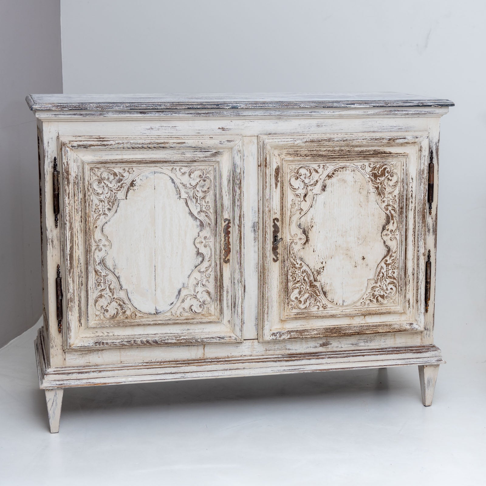 Pair of two-door sideboards made of solid walnut. The buffets stand on square tapered feet and the body is decorated with profiled moldings and panels with carved vine decoration and curved medallions. The sideboards were repainted in creamy white